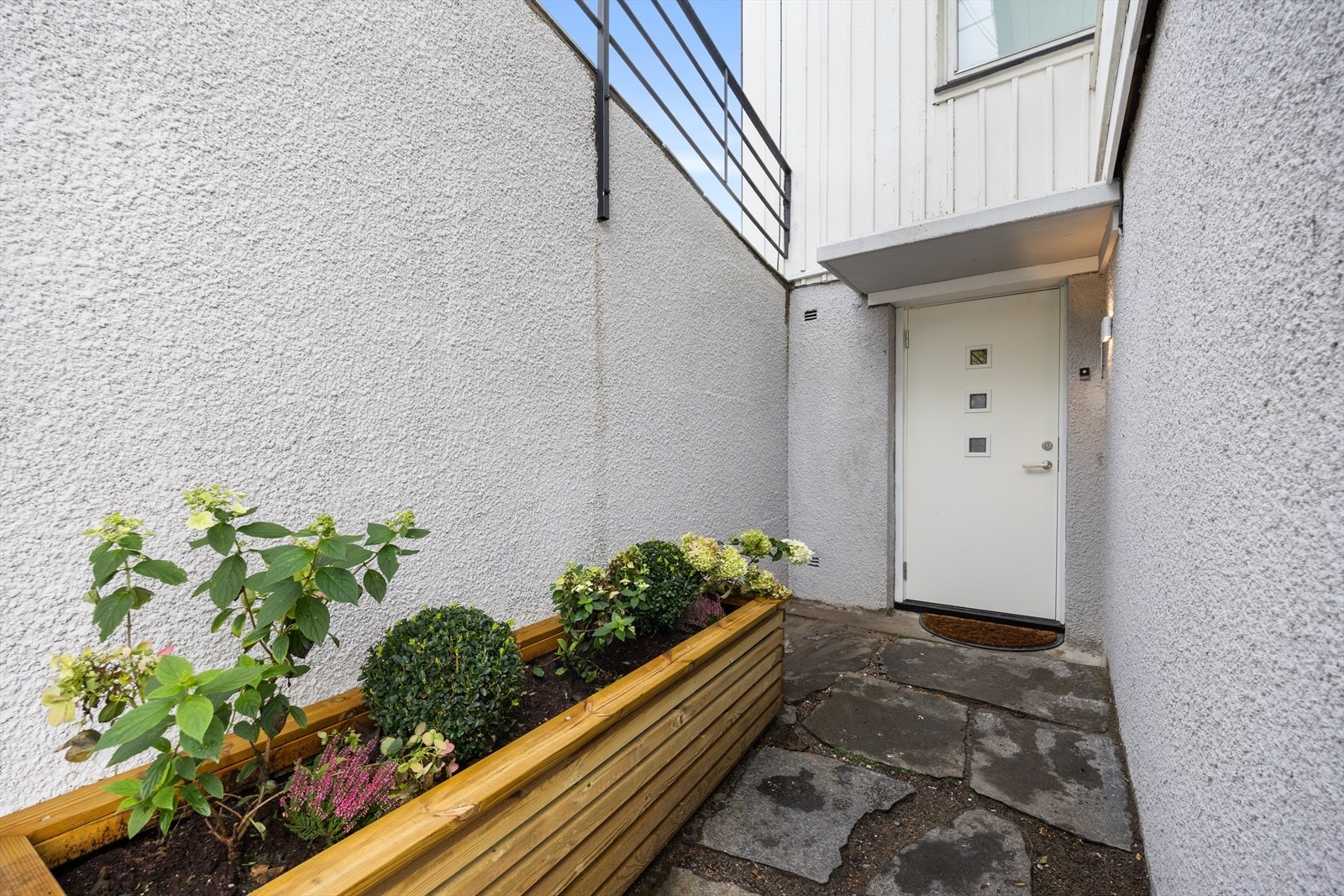 Egen inngang til leiligheten. Skiferbelagt dekke foran inngangspartiet. I tillegg er det satt opp en stor blomsterkasse med fin beplantning Galleribilde
