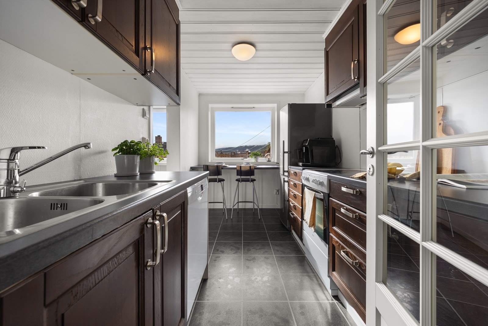 Eldre kjøkkeninnredning bestående av over- og underskap, skuffeseksjoner og frittstående hvitevarer Galleribilde