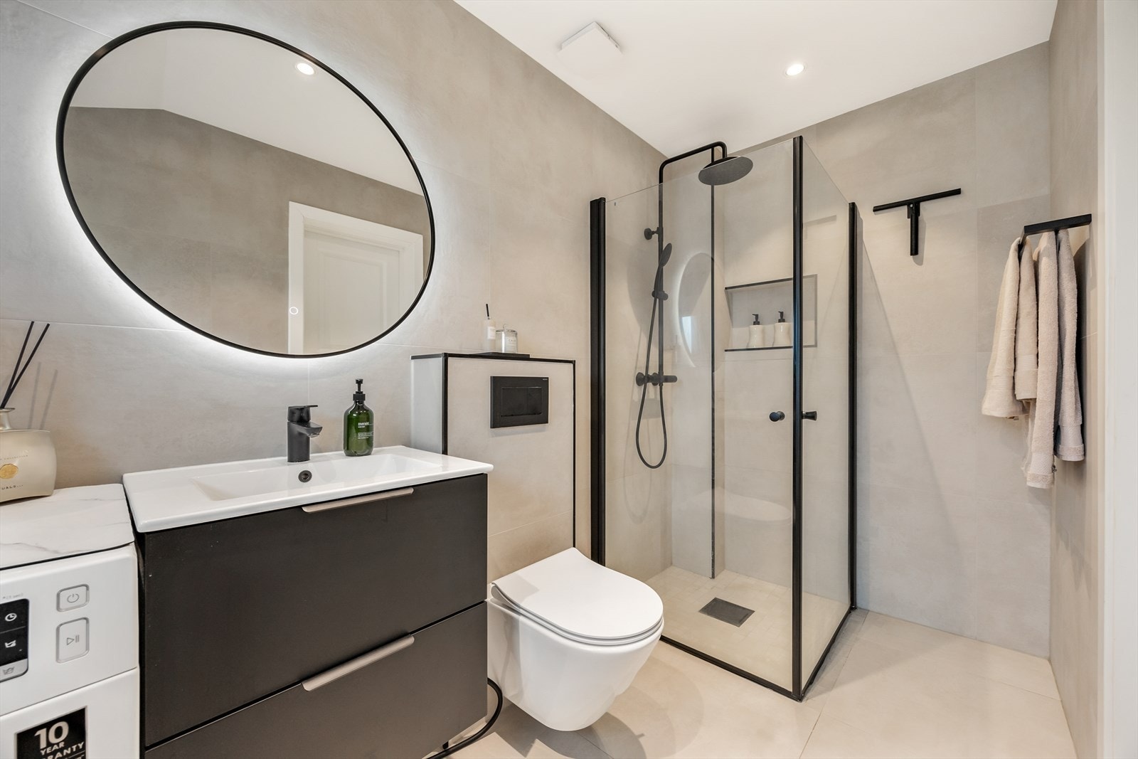 Badet er utstyrt med dusjhjørne med innfellbare glassvegger, vegghengt wc og servantinnredning med skuffer Galleribilde