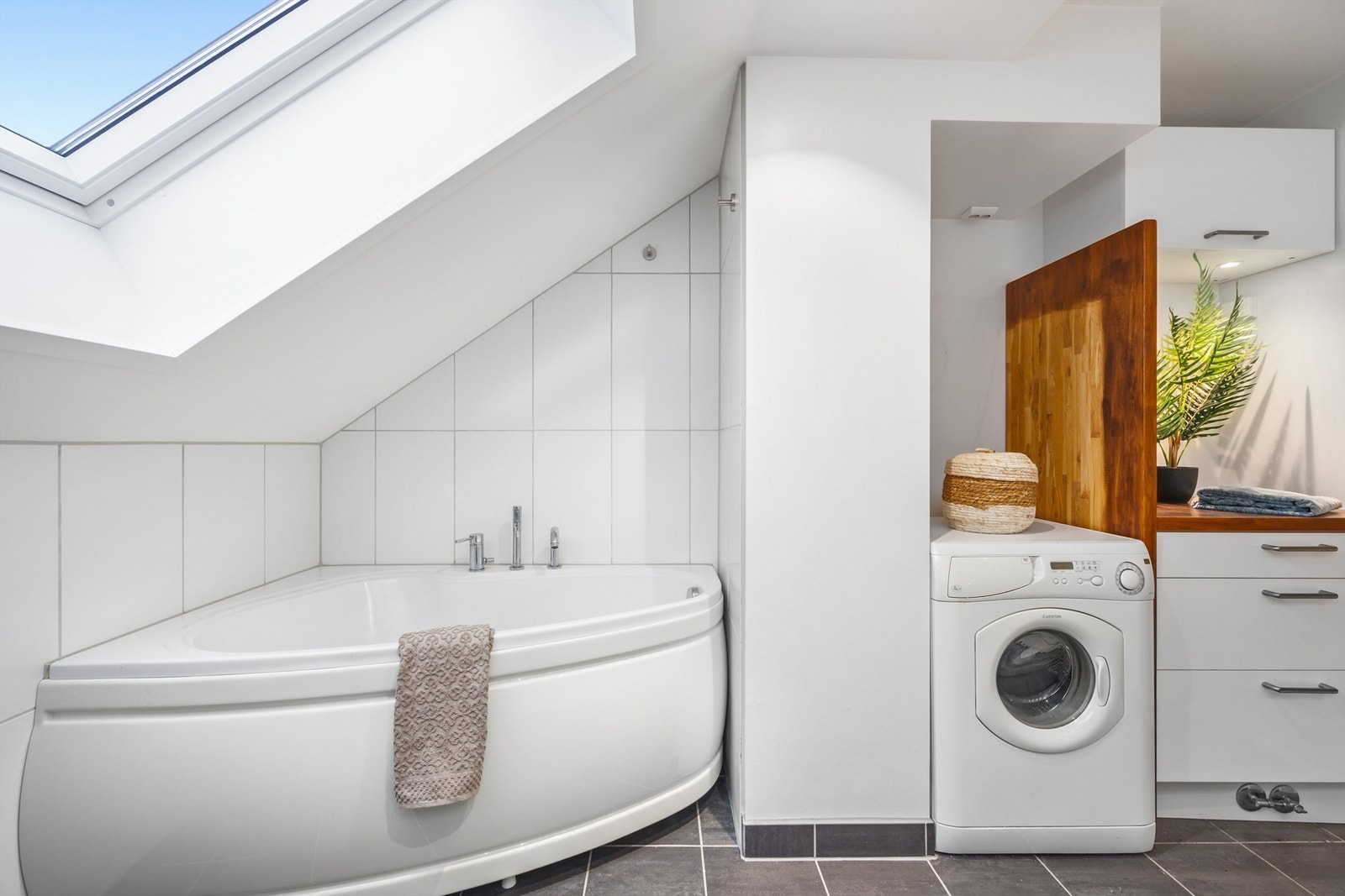 Badet er innredet med gulvstående skapinnredning med benkeplate, speil og skap med belysning på vegg over servant, samt gulvstående skuffeinnredning med benkeplate av treverk. Galleribilde