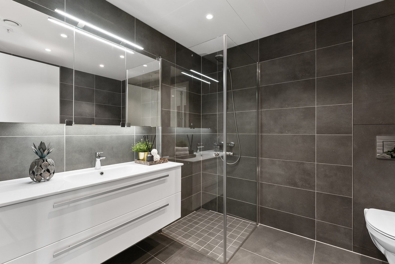 Lekkert baderom med fliser på gulv med gulvvarme, fliser på vegger og platelagt himling med downlights Galleribilde