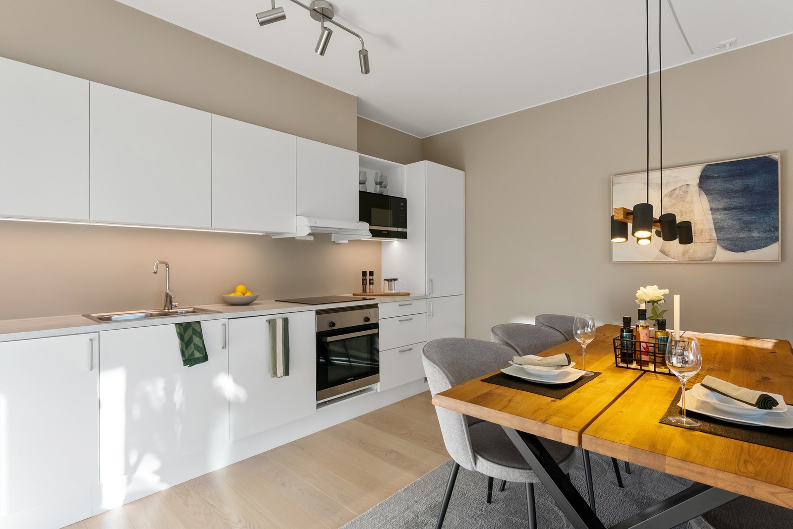 Kjøkkeninnredningen har fronter på skap og skuffer, benkeplate i laminat med nedsenket oppvaskkum og integrerte hvitevarer som induksjonsplatetopp, stekeovn, mikrobølgeovn, oppvaskmaskin og kjøleskap med frysedel Galleribilde