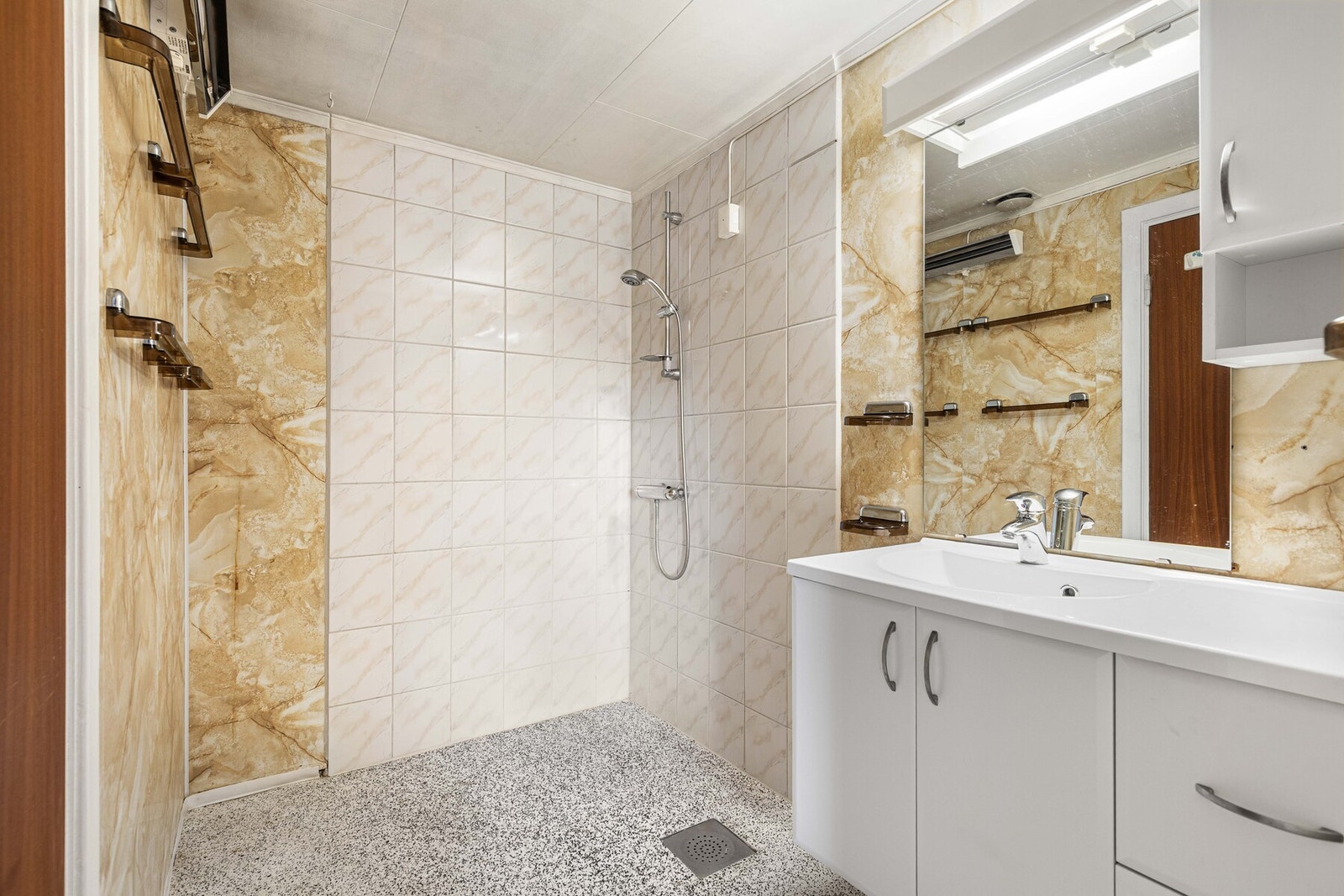 Baderom med dusj, fliser på veggene i dusjsonen, samt hvit servant med underskap og speil. Galleribilde