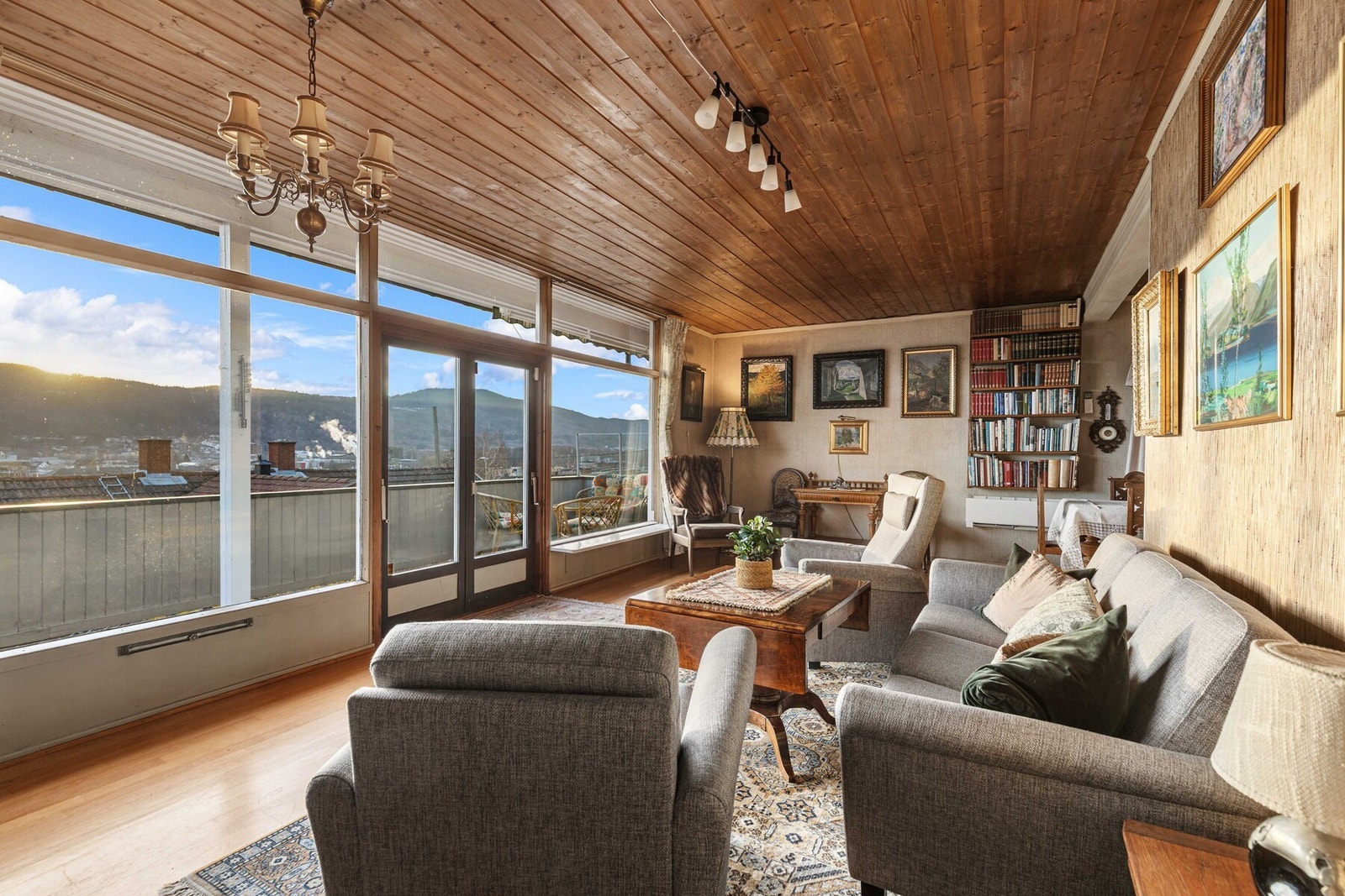 Stue med store vinduer, trepanel i tak og tapet på vegger. Galleribilde