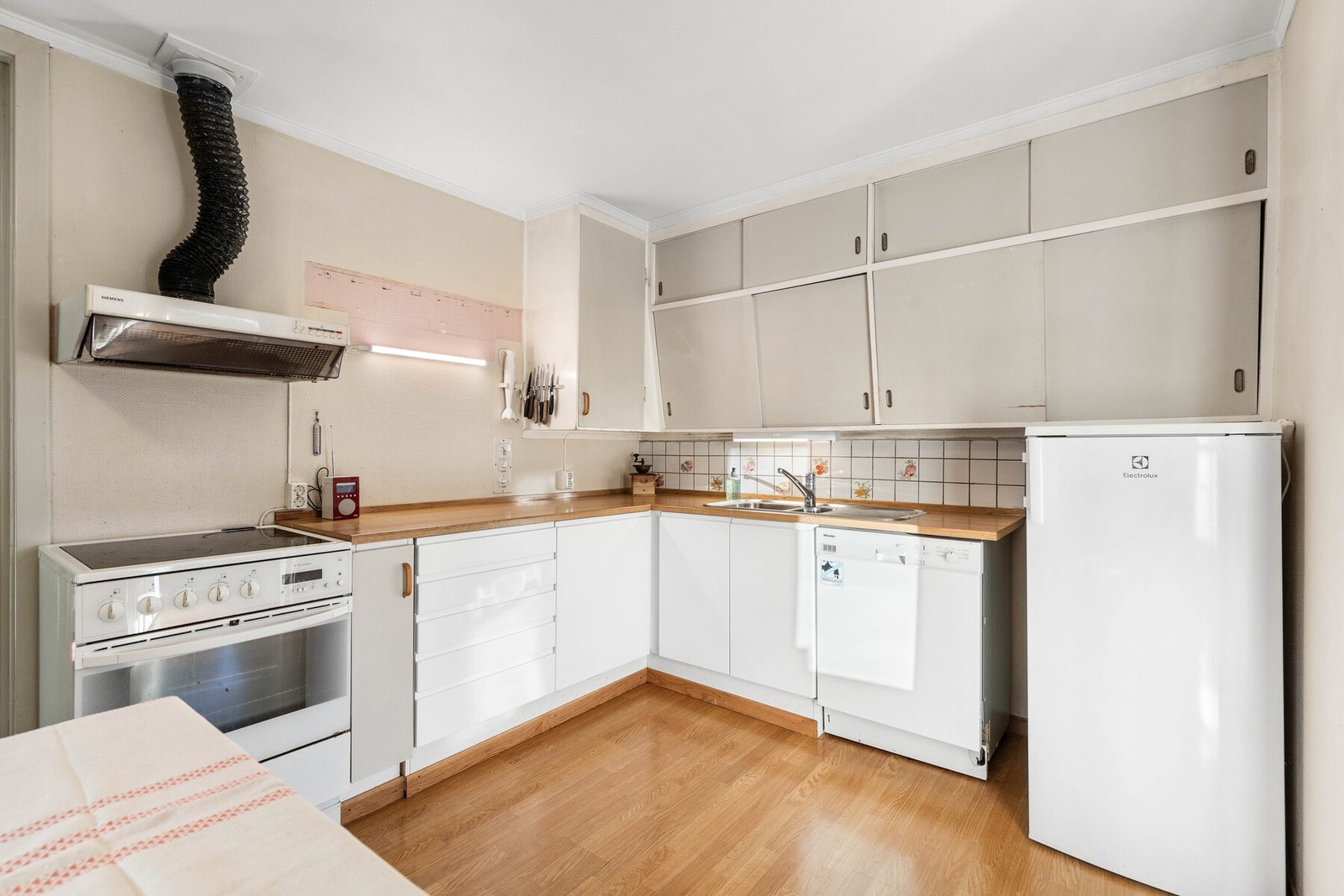 Kjøkken med hvite skapdører, benkeplate i tre og hvitevarer. Galleribilde