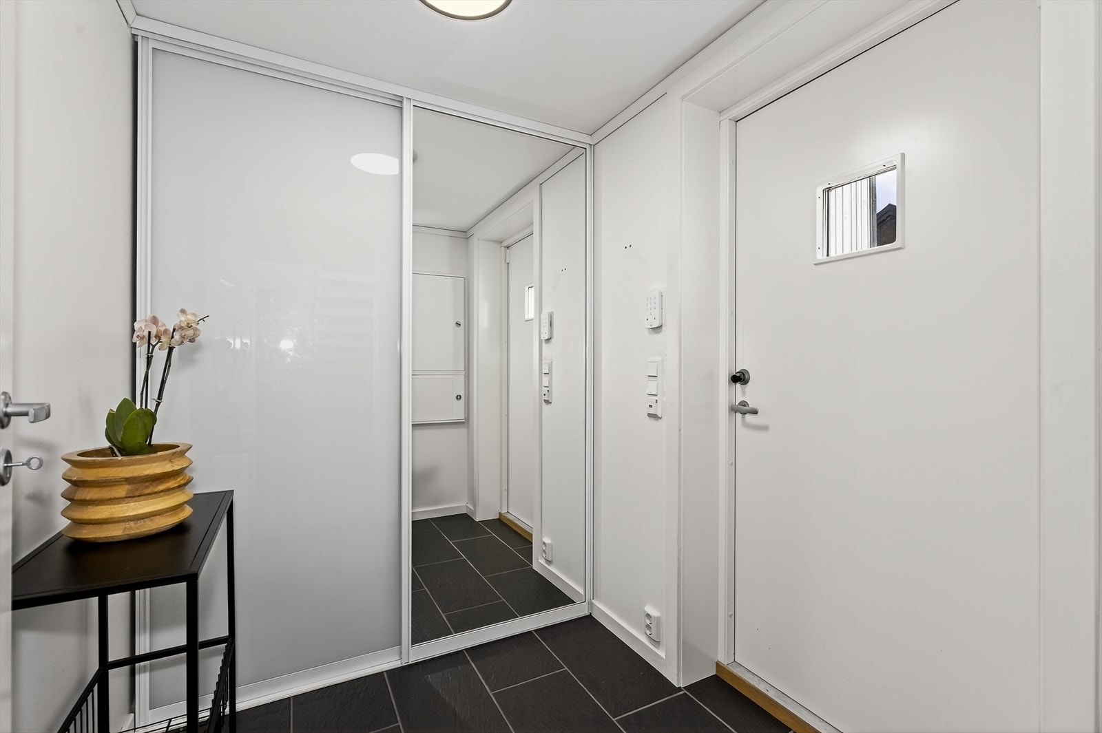 Med adkomst fra det hyggelige overbygde inngangspartiet kommer man inn i boligens gangareal hvor det er flislagt gulv og lysmalte veggoverflater. Stor skyvedørsgarderobe med speildør til sko- og ytterklær. Galleribilde