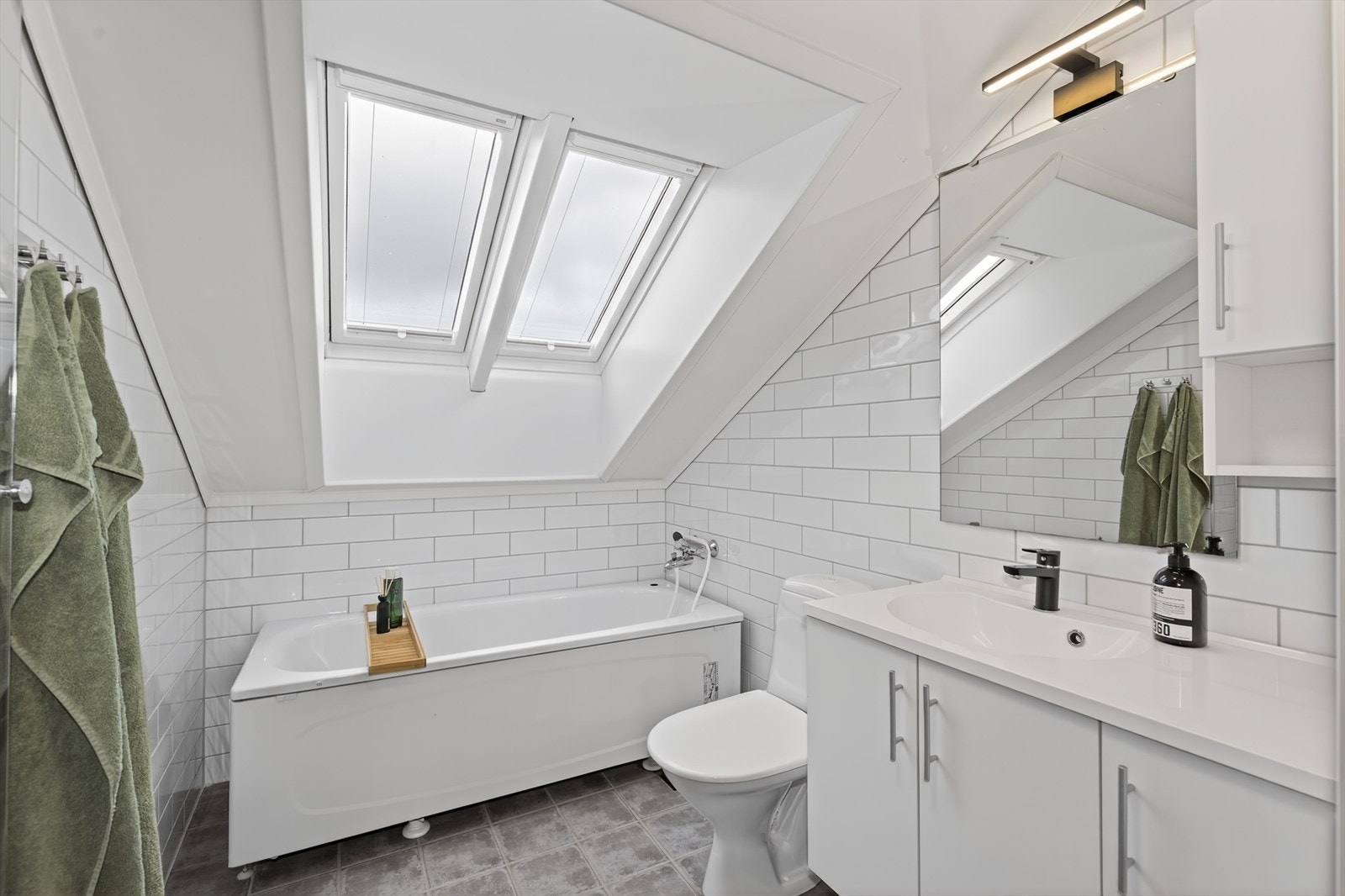 Også badet på loftetasjen er helfliset med varmekabler i gulvet, hvor takvinduene gir gode lysforhold. Badet har hvit innredning med heldekkende servant, toalett og dusjnisje med glassdør. På dette badet er det også installert badekar. Galleribilde