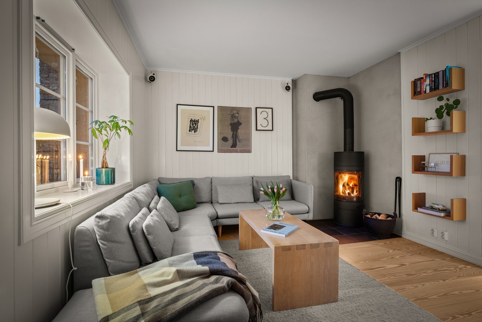 Det varme skjæret fra vedovnen sprer seg mykt i rommet og gir en lun kontrast til de lyse panelveggene og Pitch Pine-gulvet. Galleribilde