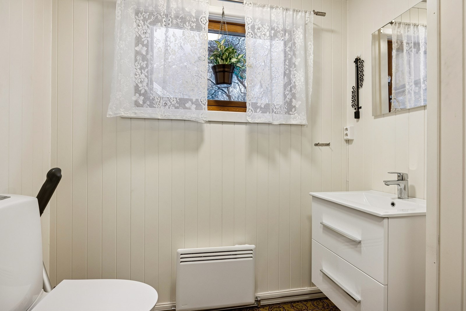 Toalettrommet er utstyrt med gulvmontert toalett og håndvask på vegg, med naturlig ventilasjon via luke i vegg. Galleribilde