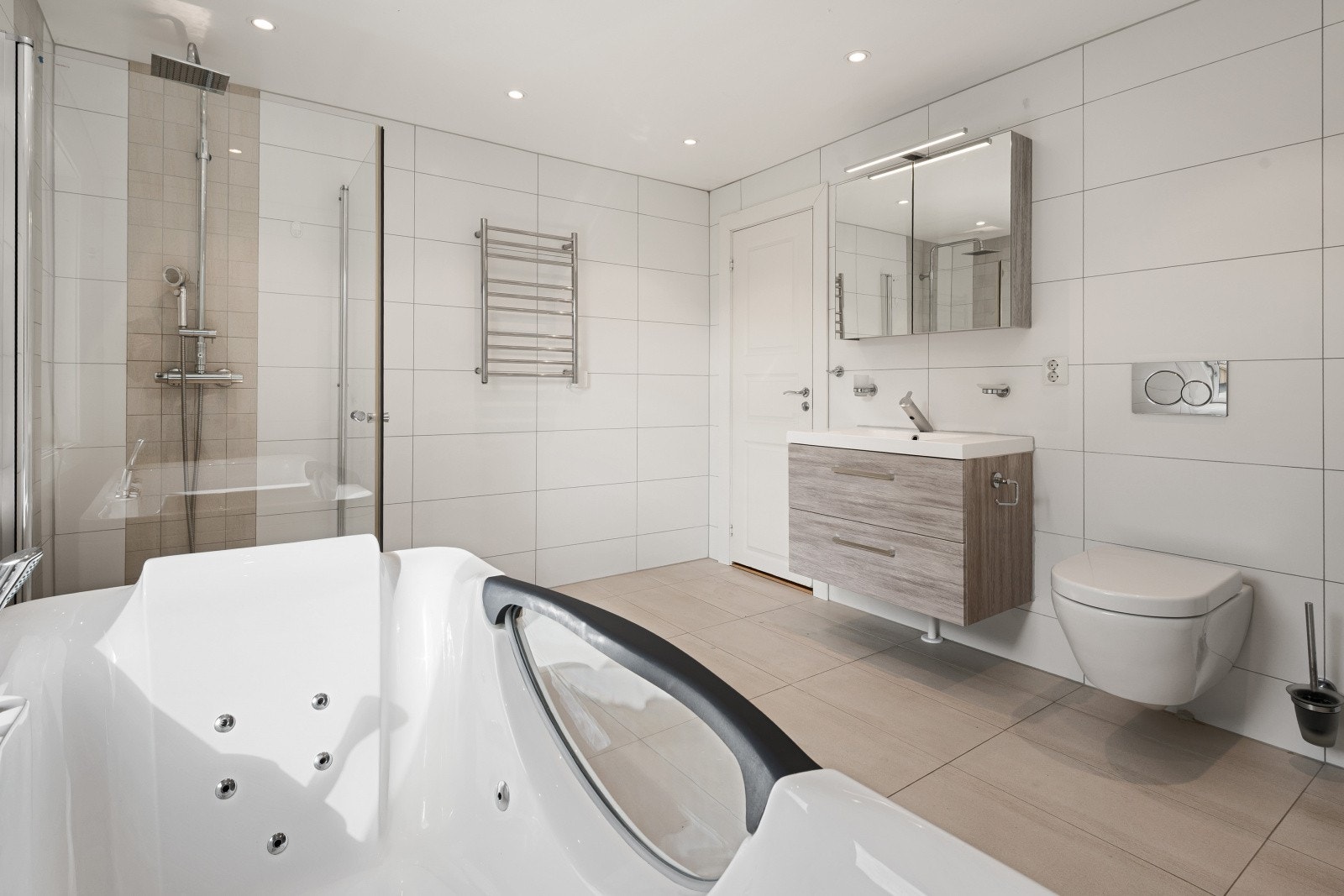 Badet er innredet med servant på skuffseksjon, speilskap med belysning, vegghengt toalett, dusjhjørne og badekar. Galleribilde