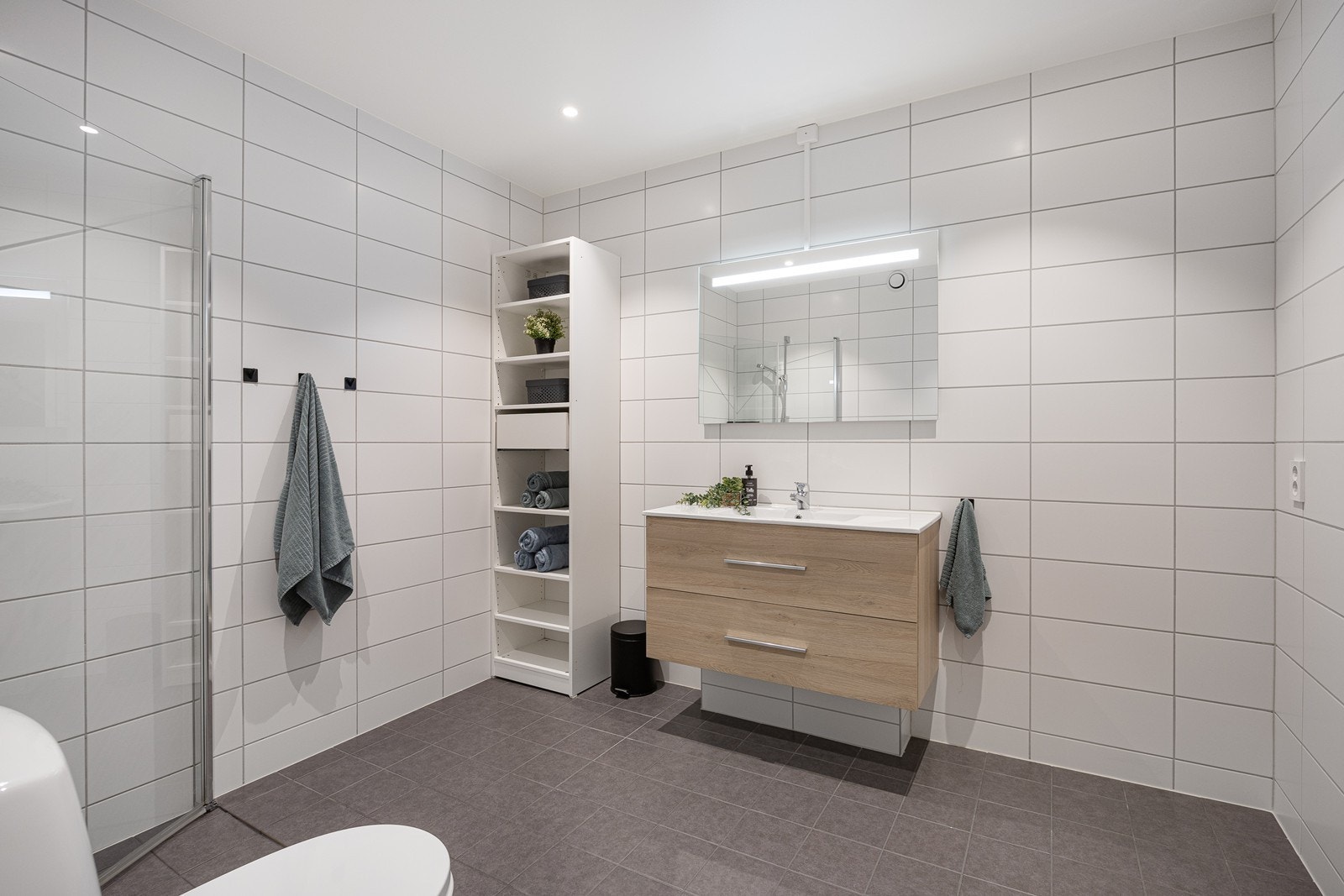 Badet er romslig, smakfullt innredet med hvite veggfliser og mørkegrå gulvfliser for en fin kontrast. Galleribilde