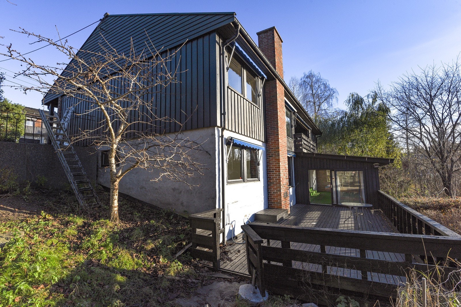 Terrassen strekker seg langs husveggen, omkranset av trær og et skjermet naturpreg. Galleribilde