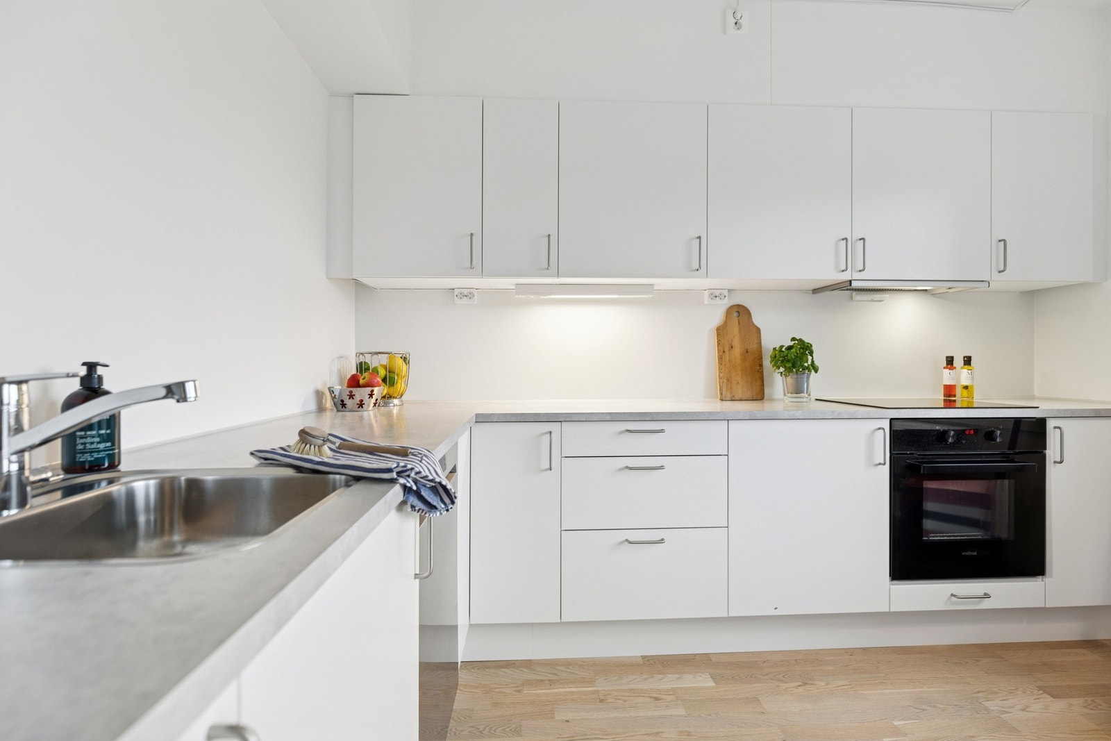 Kjøkkenet er innredet med hvite fronter, laminatbenkeplate og god belysning under overskap. Galleribilde