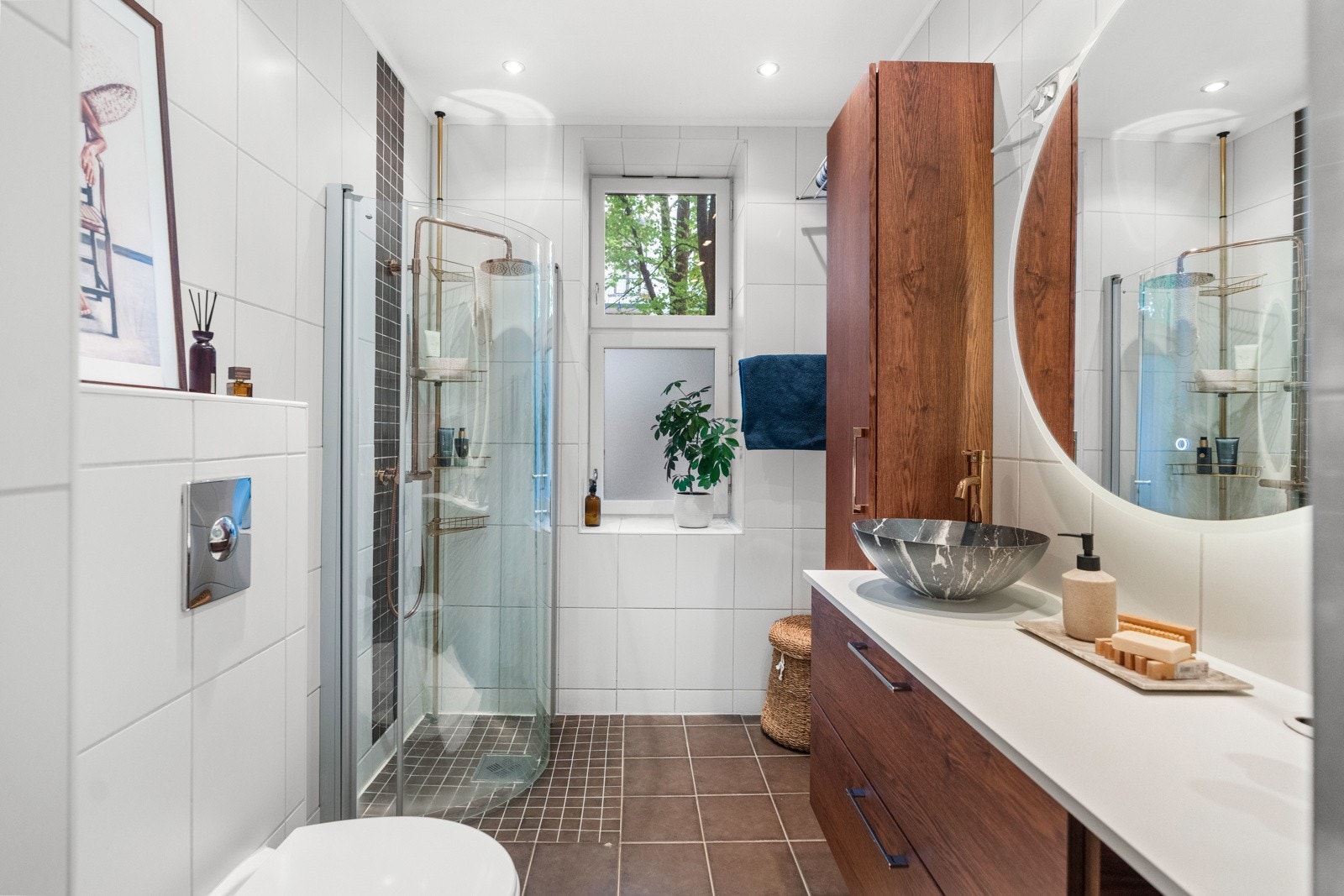 Delikat baderom med vegghengt toalett, servant med slette fronter, dusjhjørne med to svingbare glassdører og opplegg for vaskemaskin og tørketrommel. Galleribilde