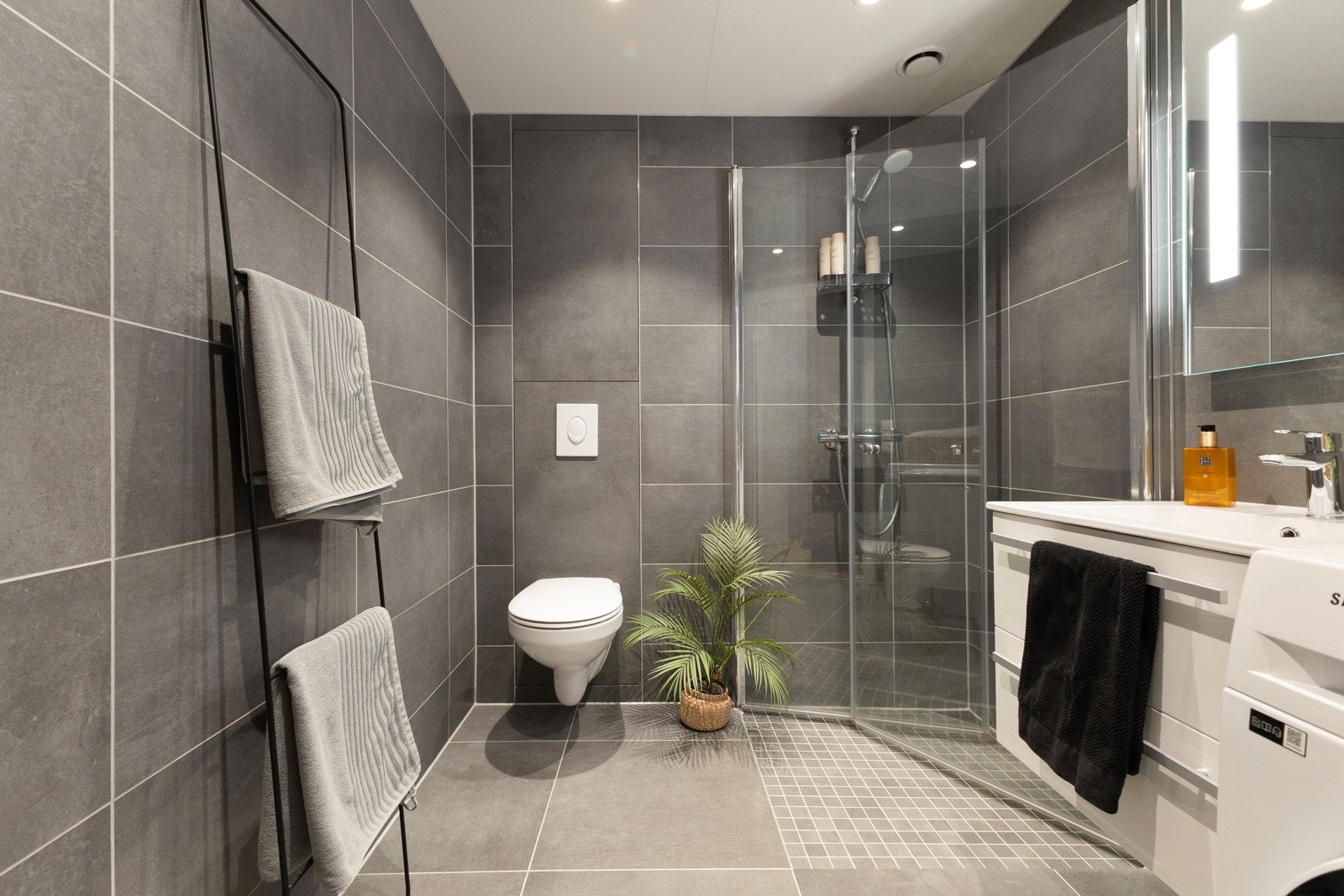 Lekkert utført og romslig baderom med store fliser, dusjhjørne med innfellbare glassdører, servant og servantinnredning med skuffer, speil med belysning over servanten samt vegghengt toalett Galleribilde