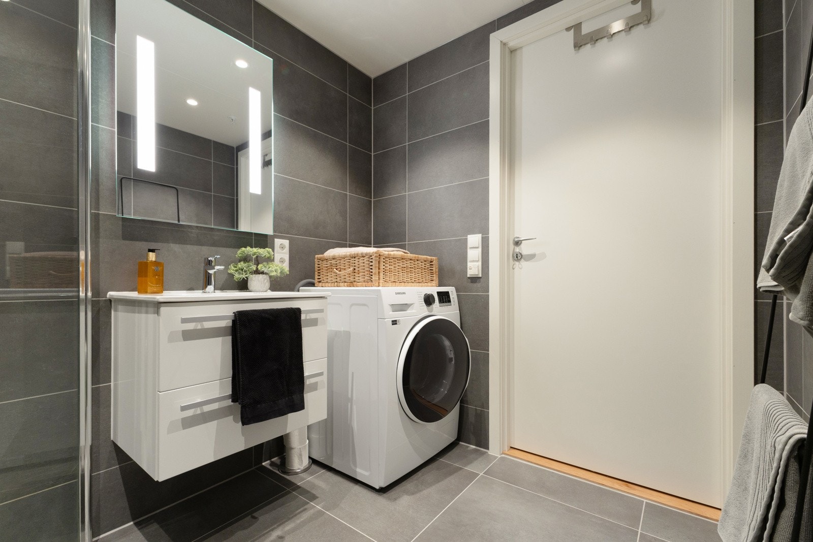 Lekkert utført og romslig baderom med store fliser, dusjhjørne med innfellbare glassdører, servant og servantinnredning med skuffer, speil med belysning over servanten samt vegghengt toalett Galleribilde