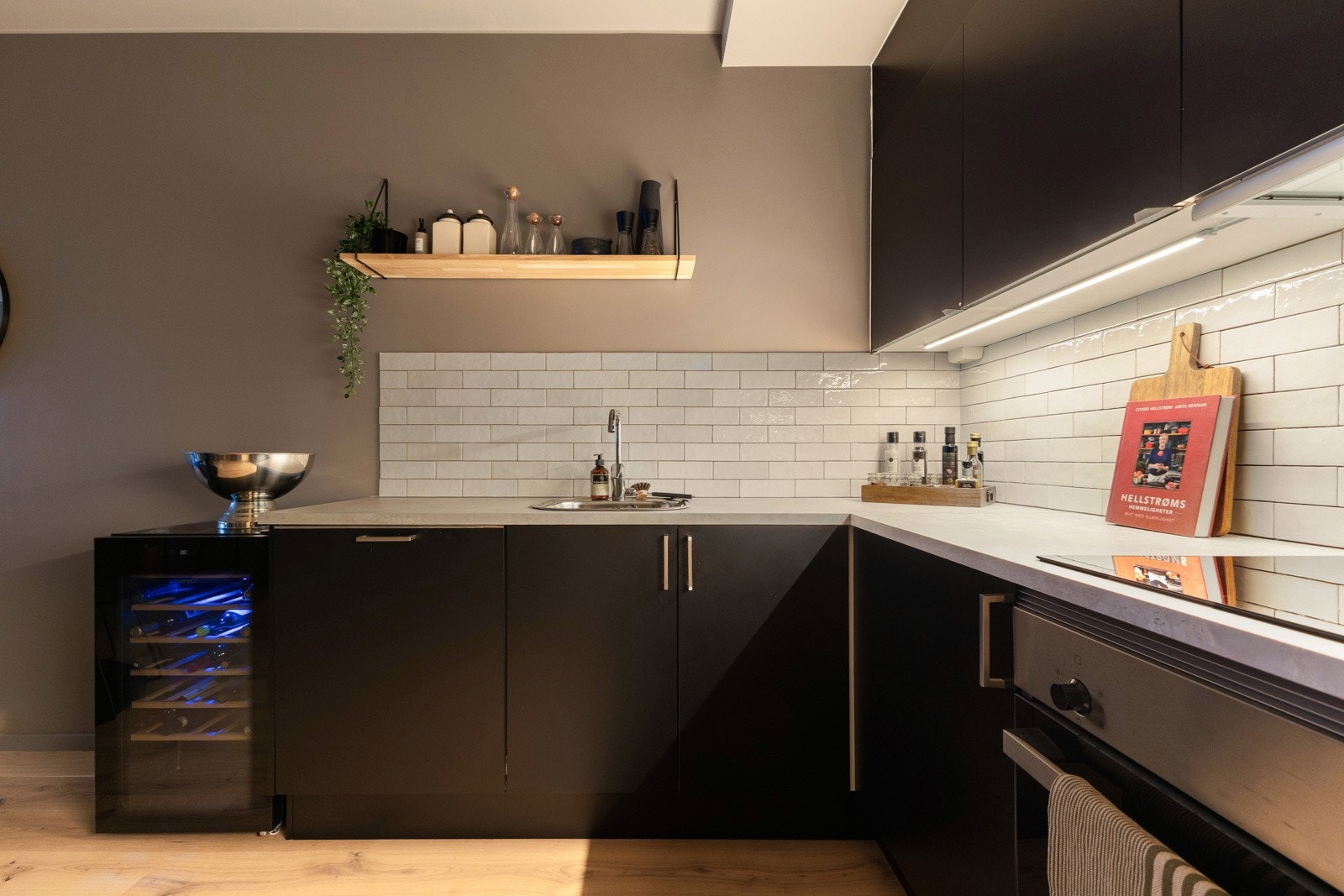 Benkeplate med nedfelt kum og induksjon platetopp samt lys under overskapene og fine fliser på vegg over benkeplaten. Galleribilde