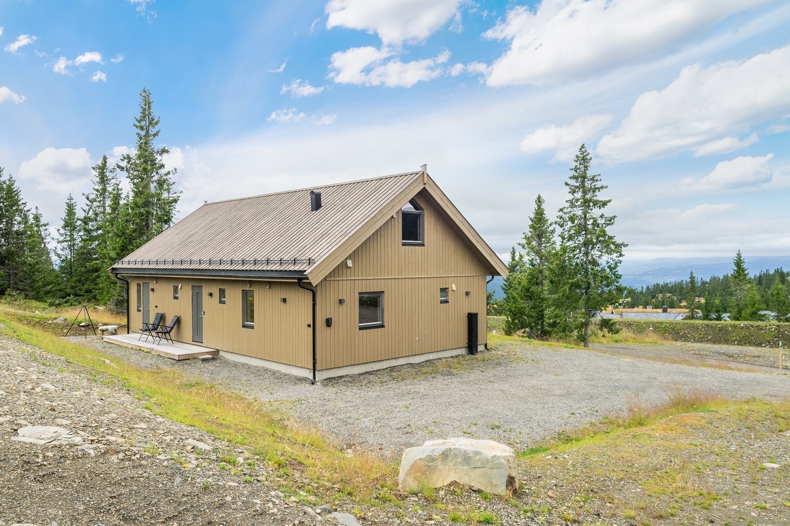 Det er god plass til flere kjøretøy på en gruslagt gårdsplass, og det er montert elbillader fra Easee på hytteveggen. Galleribilde