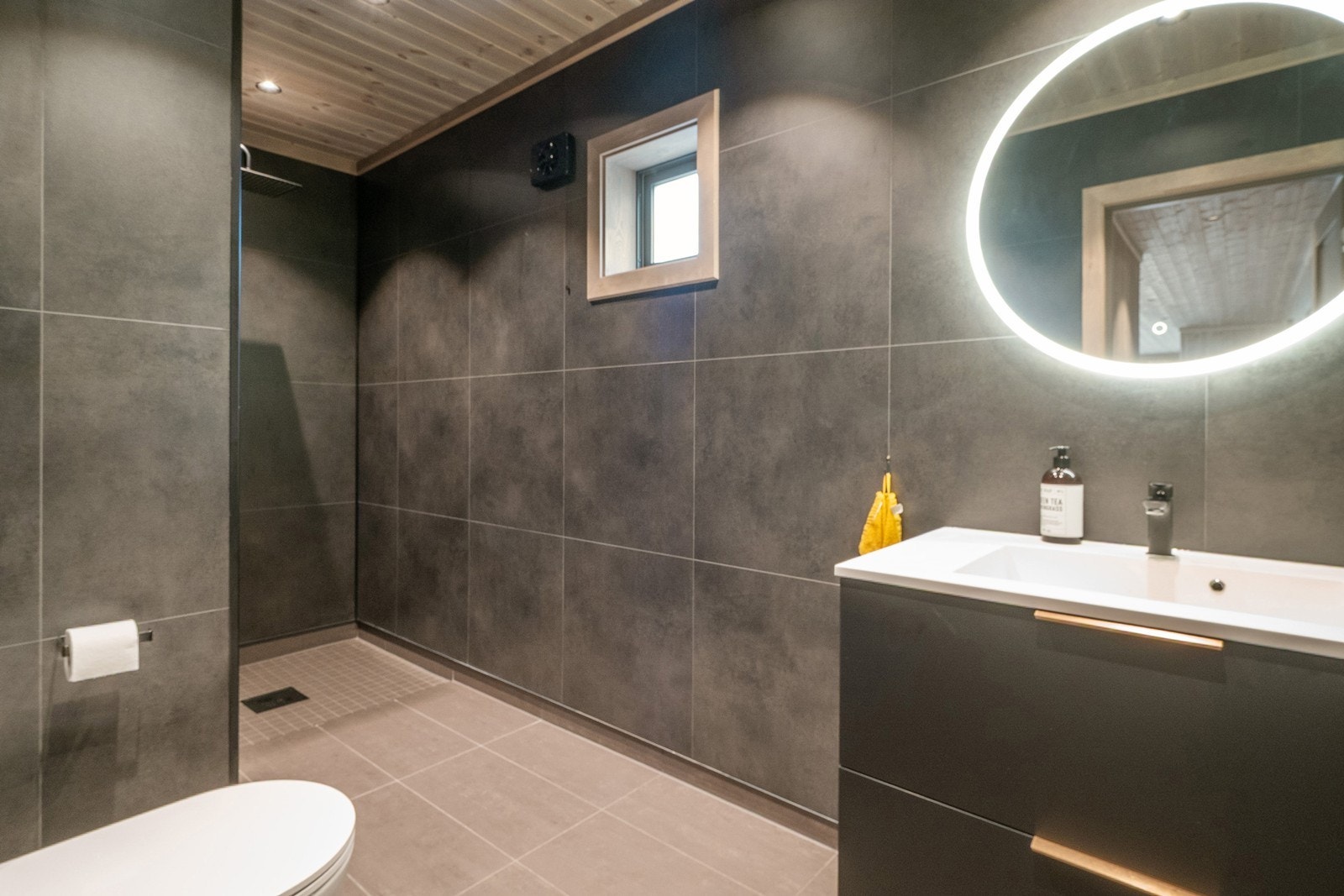 Rommet er utstyrt med lekker servant, vegghengt toalett og rengfallsdusj. Det er flislagt gulv med gulvvarme. På vegger er det våtromsplater. Galleribilde