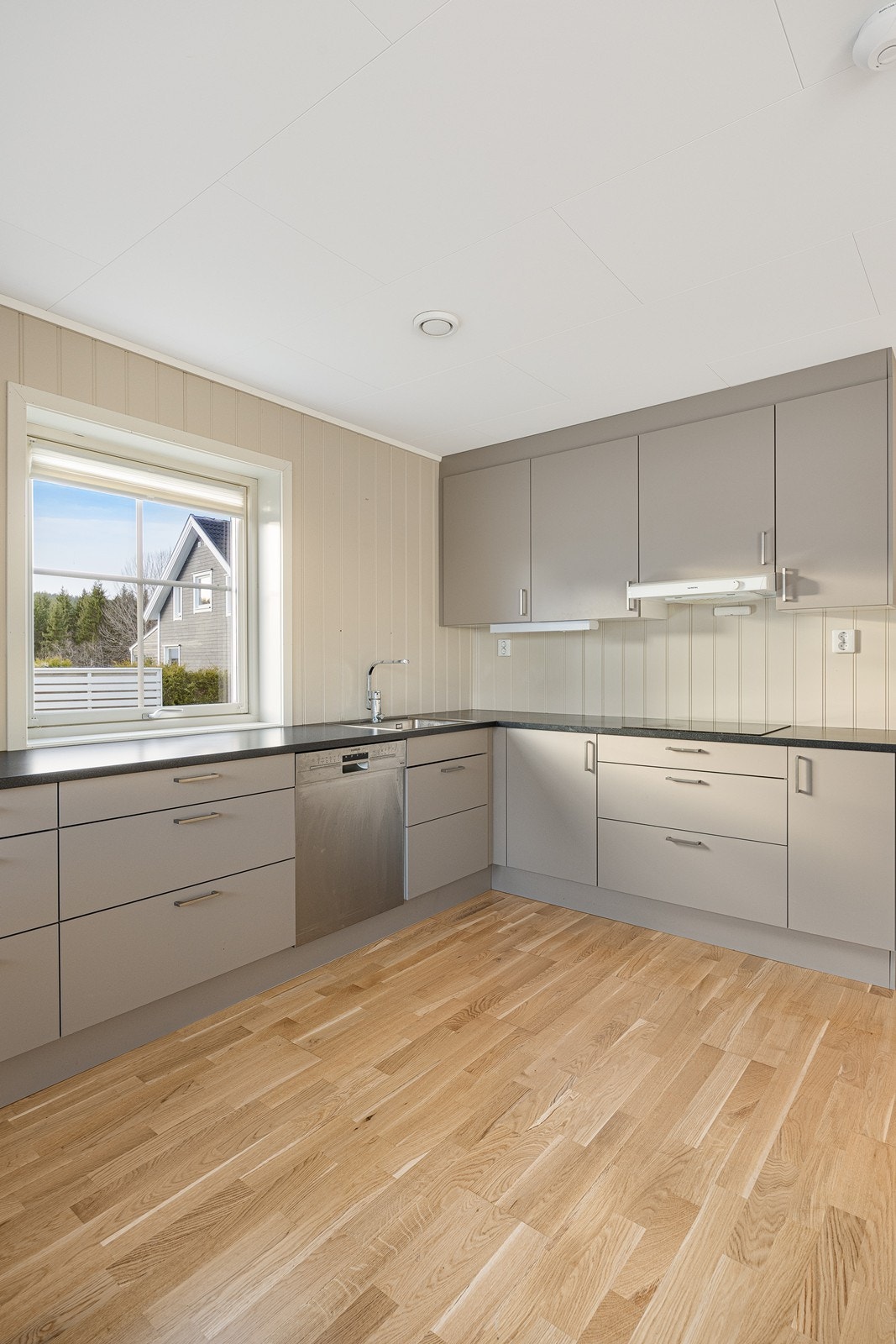 Innredningen har grå, glatte fronter, nedfelt oppvaskkum og mørk benkeplate av laminat. Galleribilde