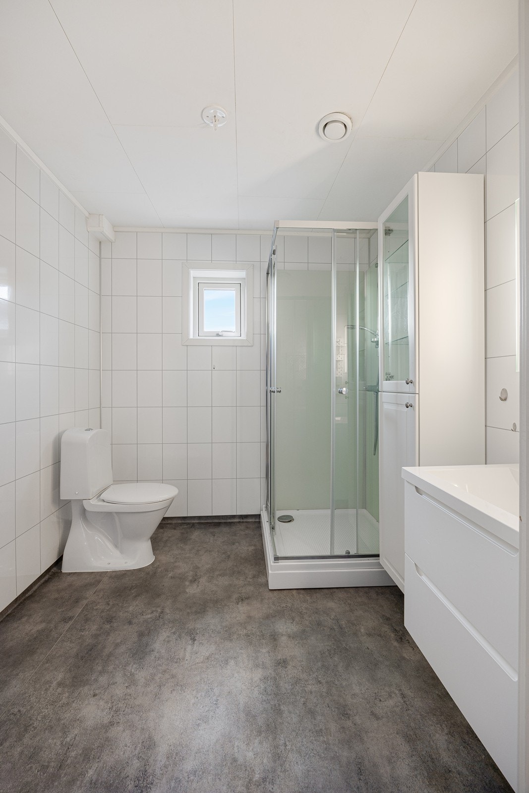 Badet er innredet med mørkt vinylbelegg på gulvet, kombinert med hvite våtromsplater i flismønster på veggene Galleribilde