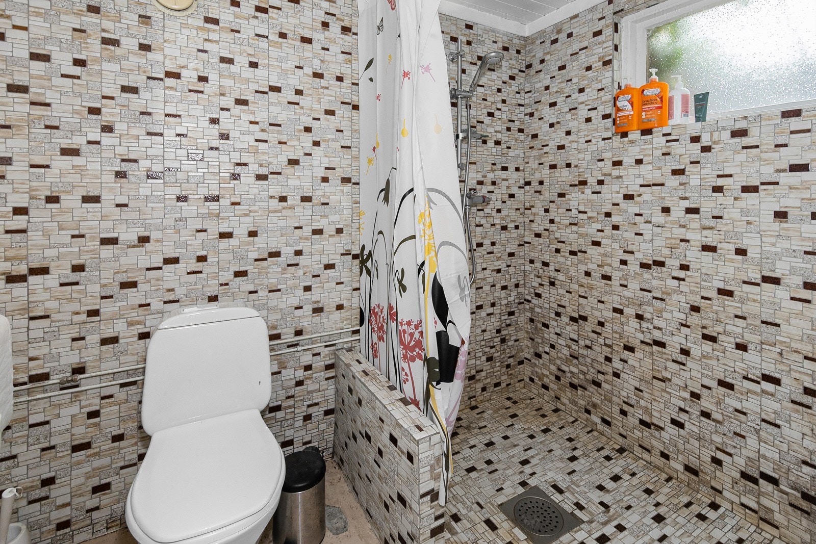 Bad med gulvmontert toalett, dusjnisje og enkel servant. Galleribilde