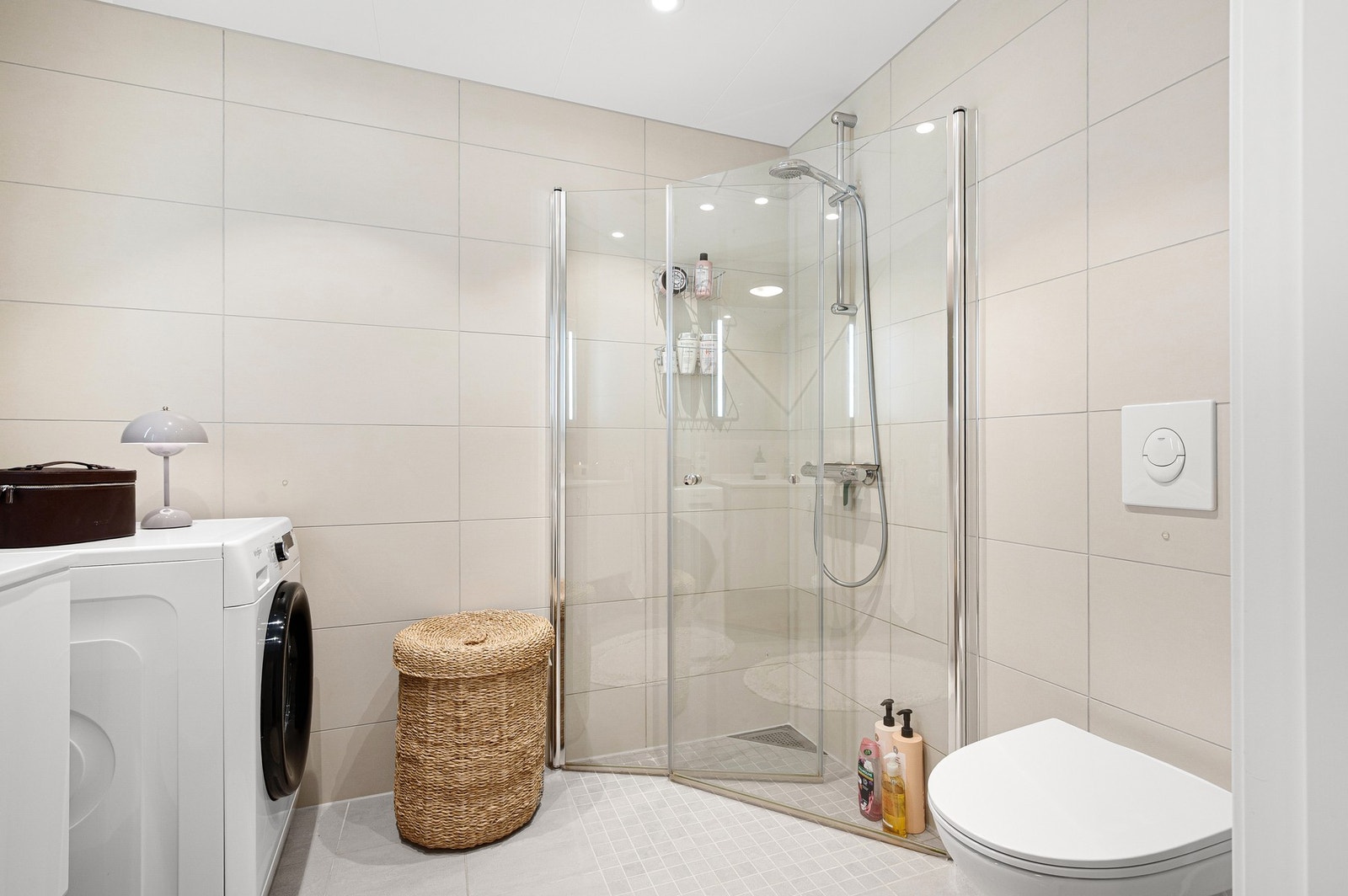 Et stilrent baderom som blant annet er innredet med toalett, dusj, servant med underskap og speil Galleribilde