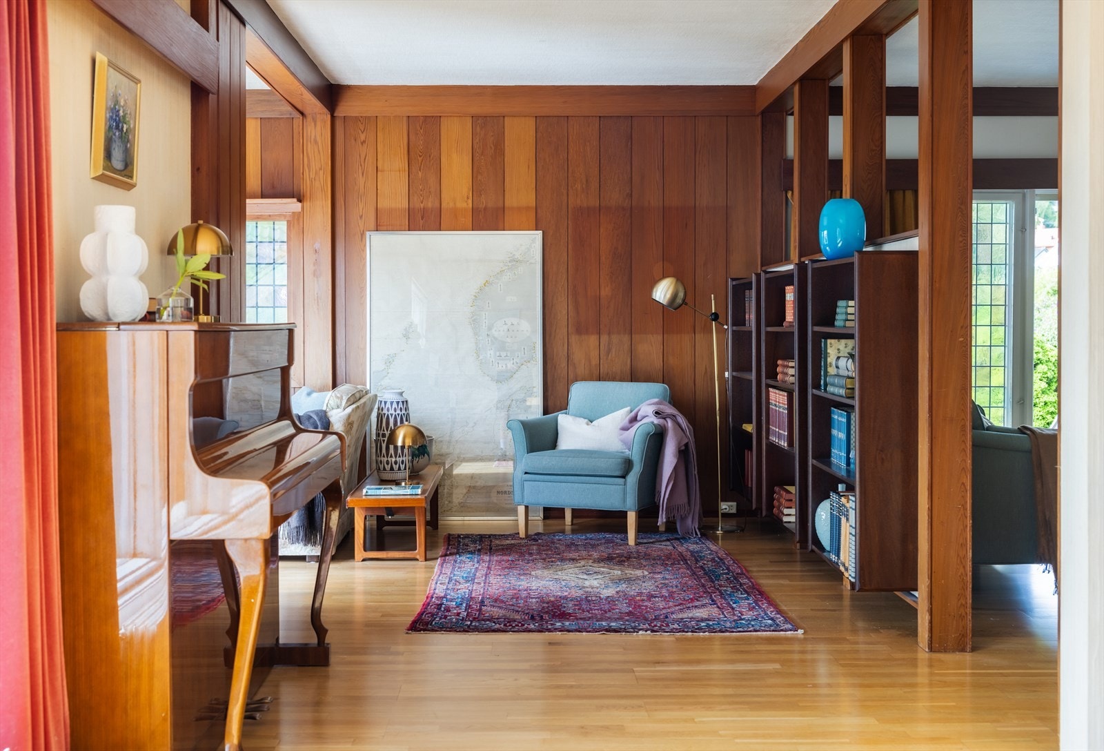 Stuen fremstår lun og koselig, i tidstypisk stil med delvis gyllen redwoodpanel og malt strietapet på vegger. Galleribilde