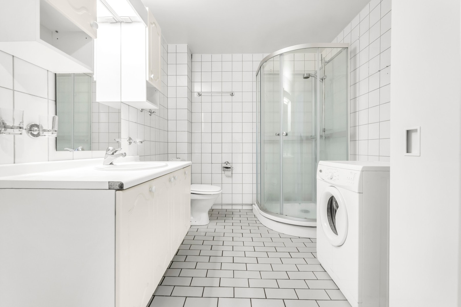 Flislagt bad med wc, dusjkabinett, innredning og vaskermaskin. Galleribilde