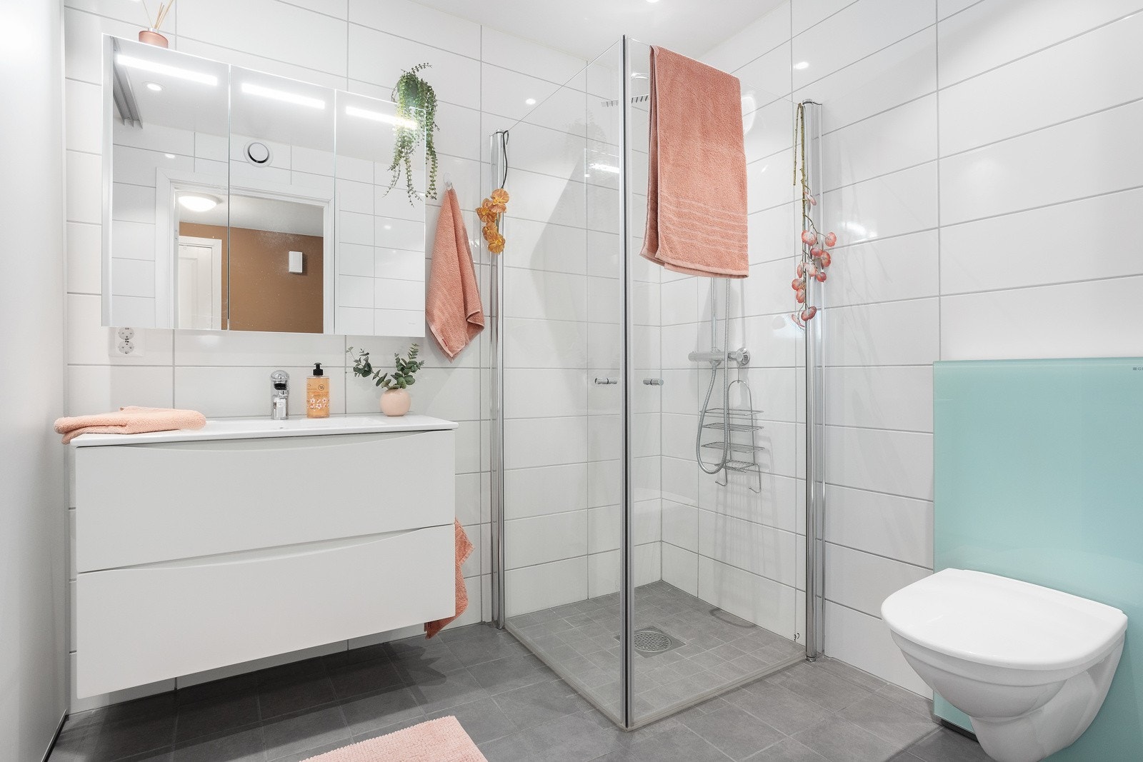 Flislagt bad med dusjdører i glass. Speilskap med oppbevaring. Galleribilde