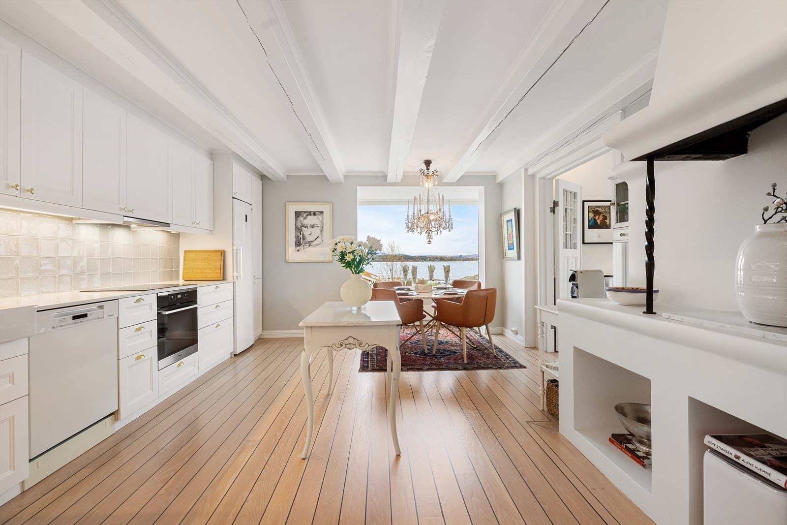 Kjøkkenet har profilerte fronter med påkostede beslag og håndtak. Benkeplaten er i komposittstein med dobbel porselensvask og ettgreps kjøkkenarmatur i kobber/gull. Mellom benkeplate og overskap er det flislagt veggflate. Galleribilde