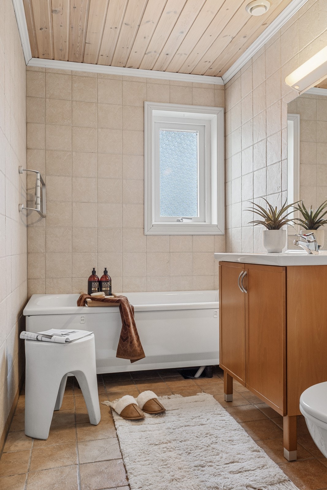 Badet i 1 etg. er antatt fra byggeår med flislagte overflater og gulvvarme. Utstyrt med servantskap, gulvmontert toalett og badekar med veggmontert blandebatteri og hånddusj. Galleribilde