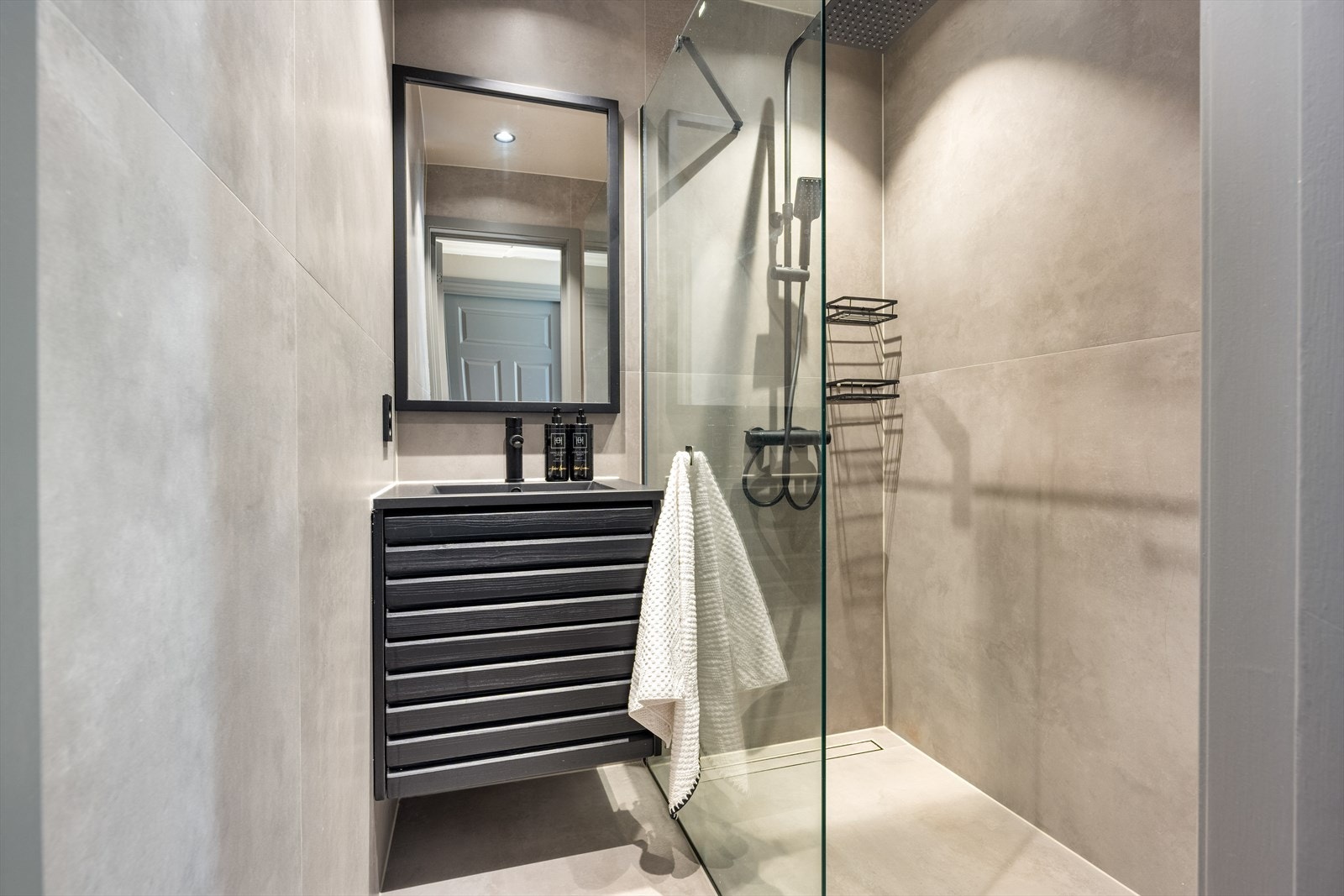 Bad med delikate store fliser, behagelig gulvvarme og elegante detaljer i sort Galleribilde