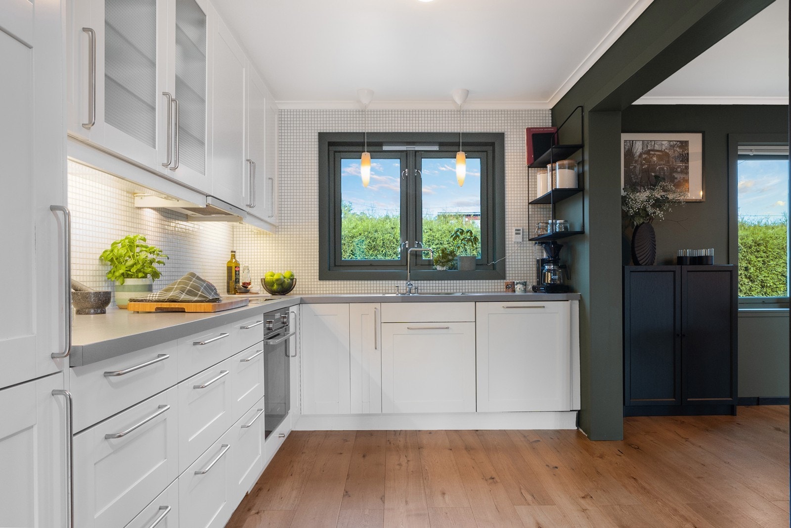 Et vindu som vender mot gårdsplassen slipper inn fint dagslys, mens lyse mosaikkfliser over benk og belysning under overskapene gir rommet et lyst uttrykk. Galleribilde