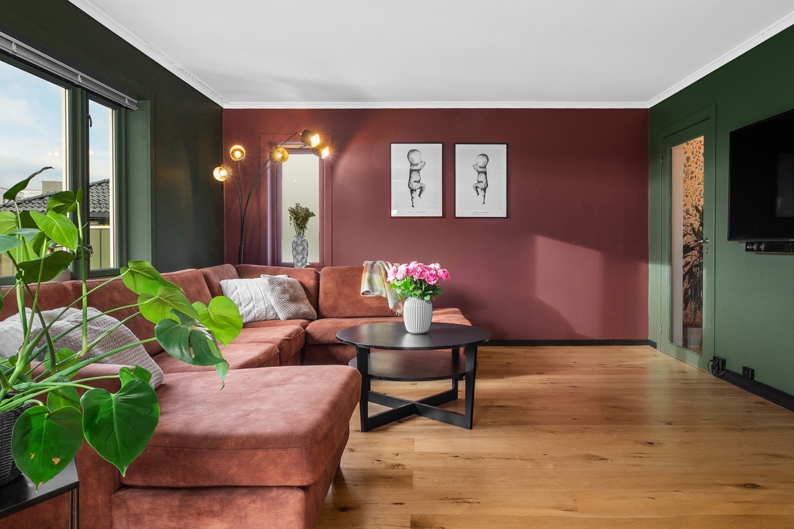 Boligens stue fremstår innbydende, med en harmonisk fargepalett som skaper et lunt preg. De grønne og burgunderrøde veggene står i kontrast til parkettgulvet i eik fra 2020. Galleribilde