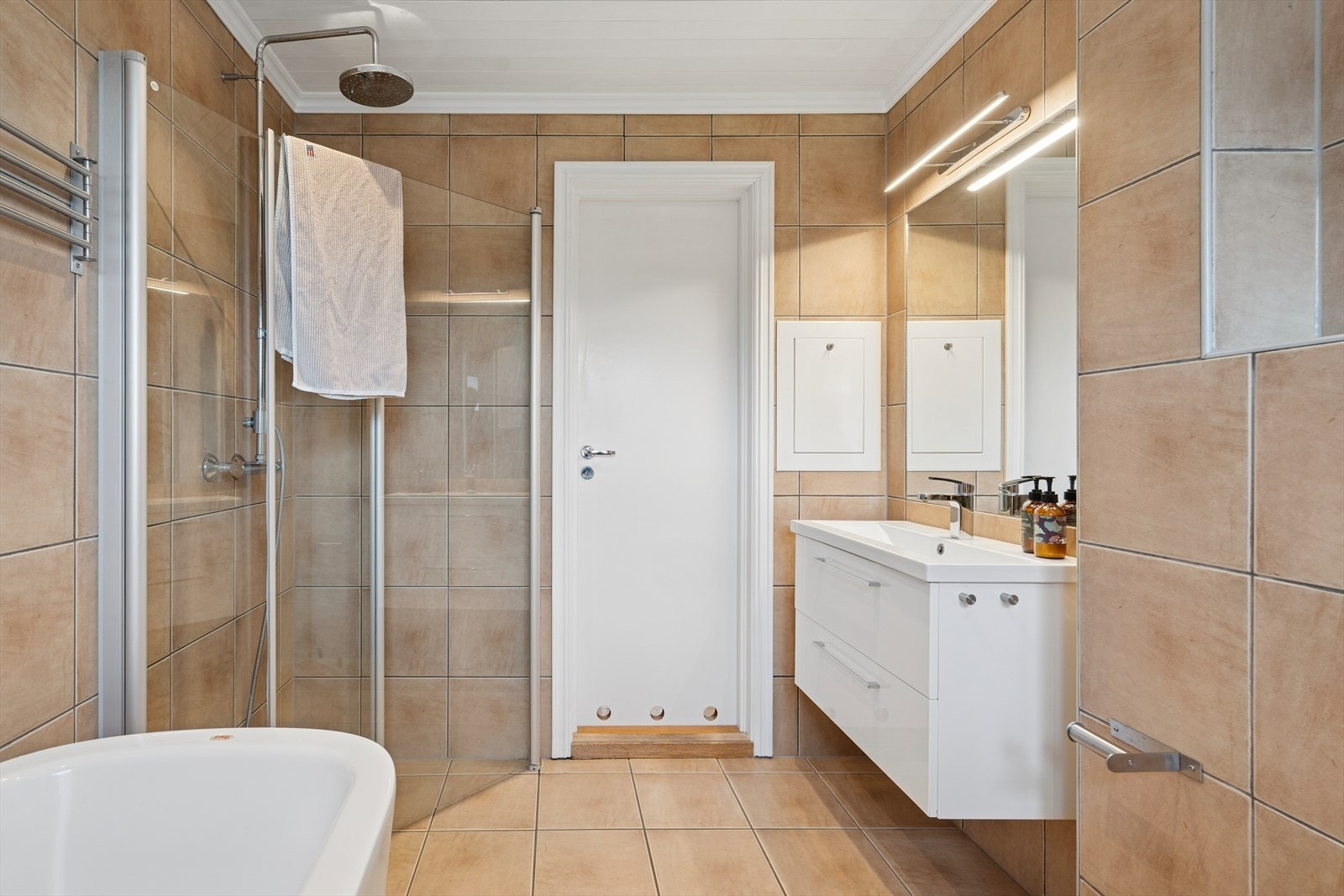 Badet er utstyrt med innredning med nedfelt servant fra 2017, vegglimt speil, vegghengt toalett, bidé, dusjhjørne med glassvegger og badekar. Galleribilde