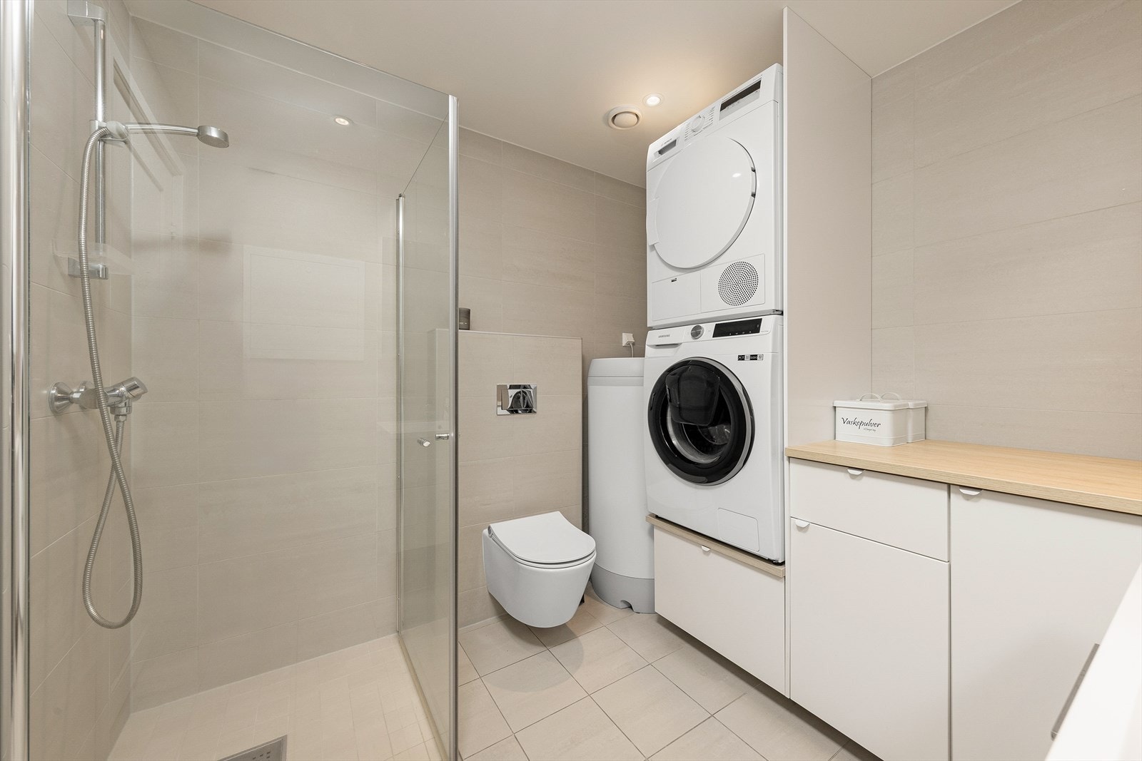Pent bad/vaskerom med dusjhjørne, vegghengt toalett, smart vaskerominnredning og lys baderomsinnredning. Galleribilde