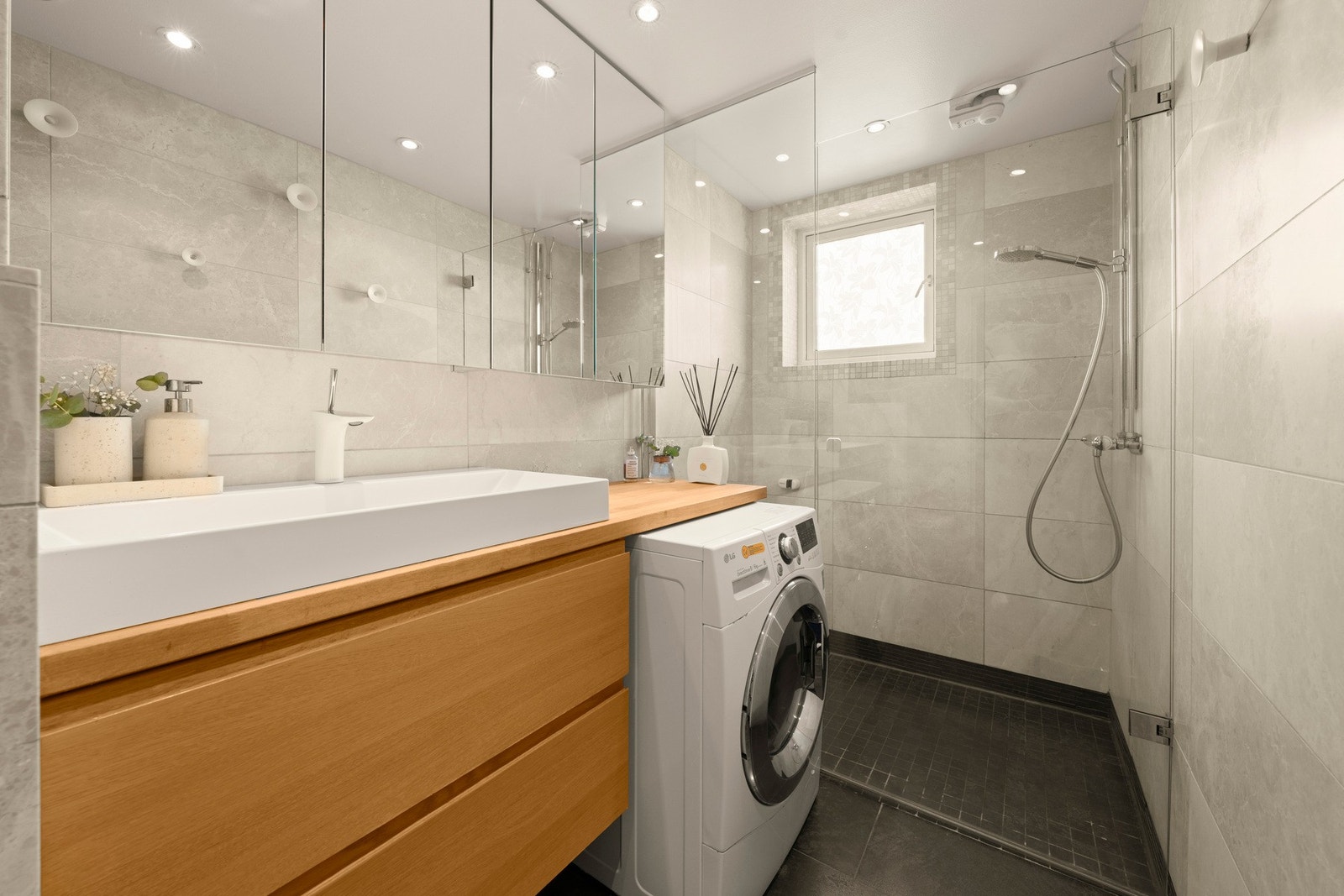 Badet er utstyrt med vegghengt toalett, dusj med glassvegg, servant i praktisk innredning og opplegg for vaskemaskin Galleribilde