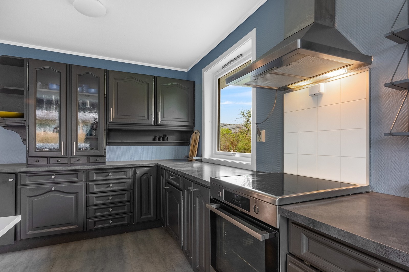 Innredningen har profilerte fronter malt i mørkt med delvis vitrineskap og hyller, benkeplate i laminat og beskyttelsesplater i steke- og vaskesoner. Galleribilde