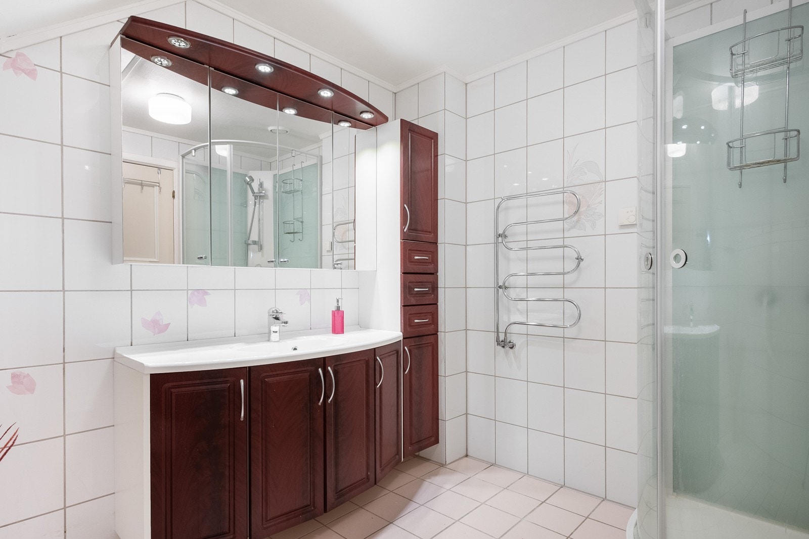 Badet ligger i 2. etasje med flislagte overflater, dusjkabinett, skap- og skuffeinnredning med nedfelt servant og tredørs speilskap. Galleribilde