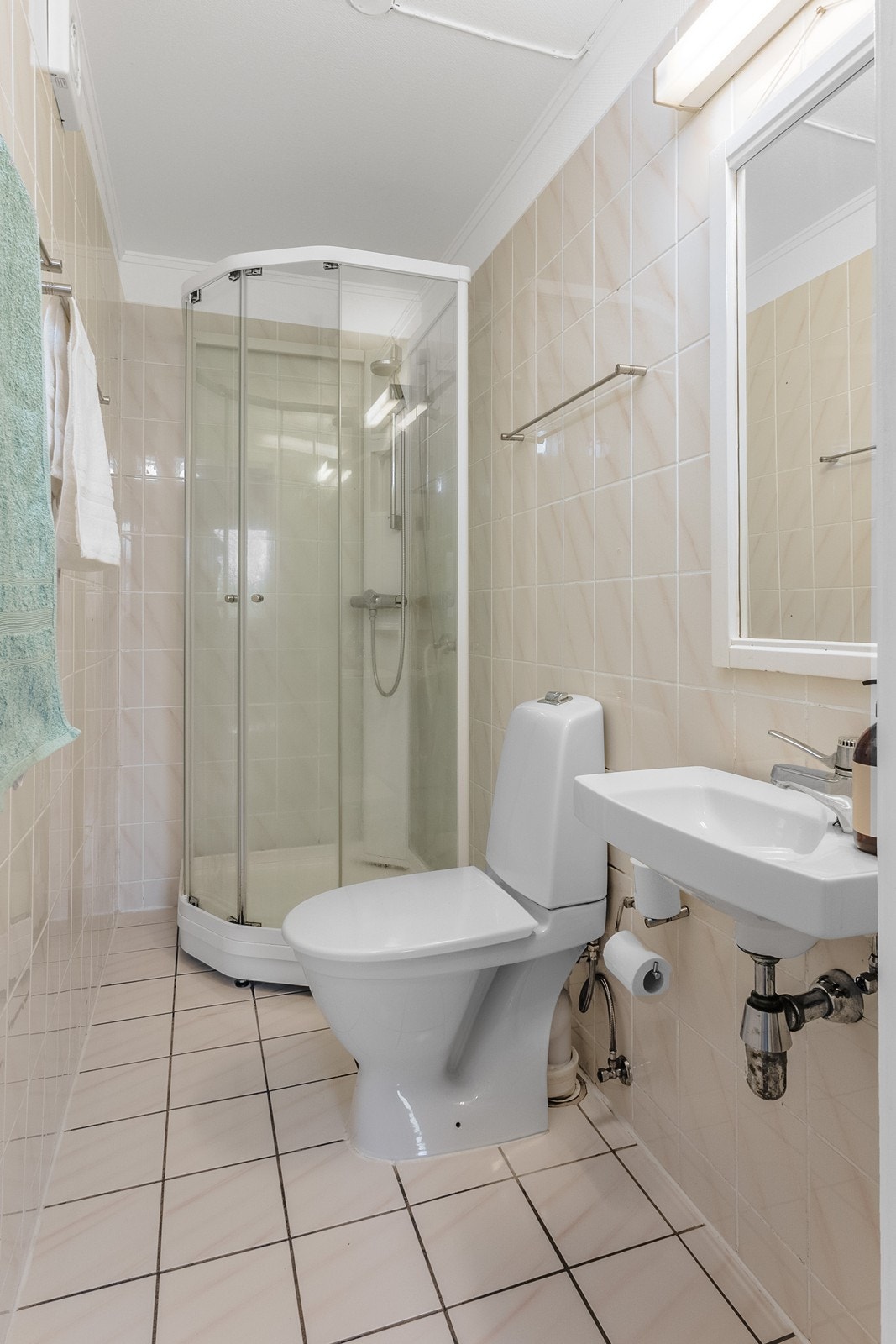 Badet har flislagte overflater og er innredet med dusjkabinett, toalett og enkel, vegghengt servant. Galleribilde