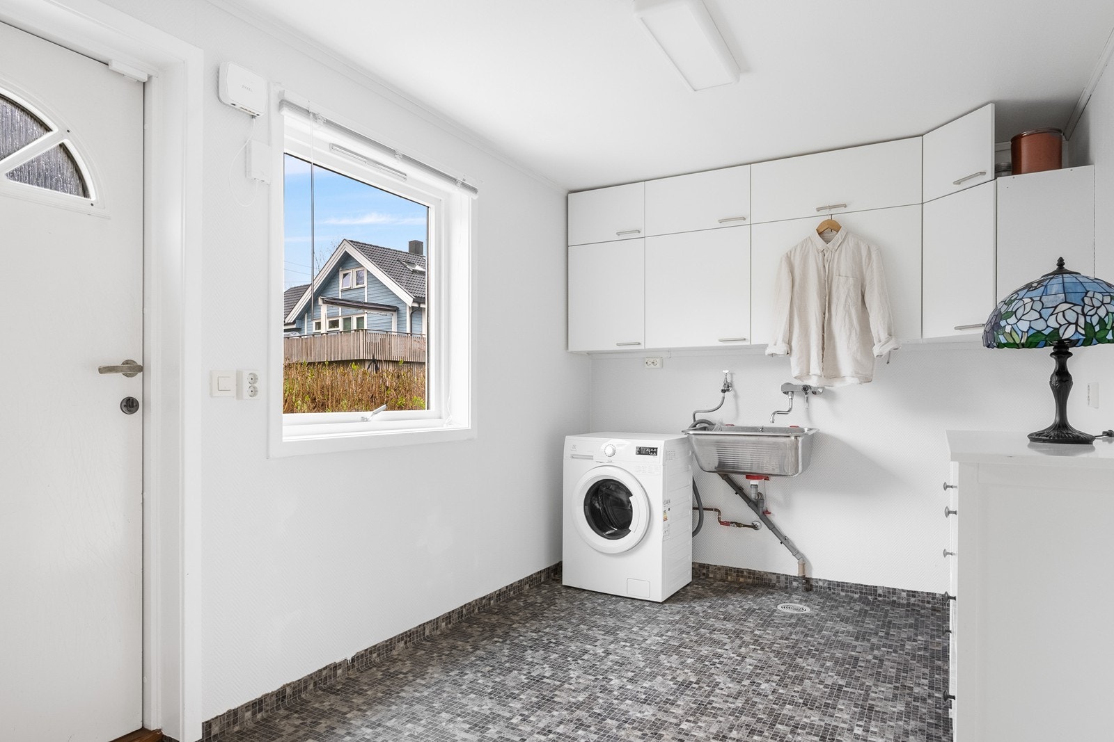 For klesvask har hoveddelen vaskerom i 1. etasje med mosaikkflis på gulv, utslagsvask, opplegg for vaskemaskin og overskap for oppbevaring, samt direkte utgang til boligens nordside. Galleribilde