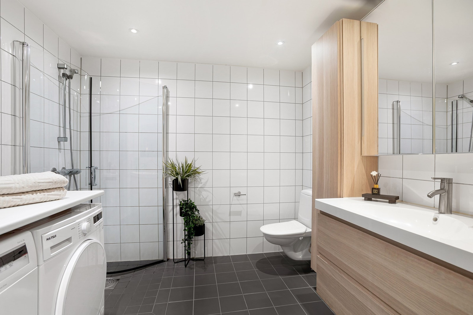 Dusjbad/wc - dusjhjørne med innfellbare glassdører og to-greps armatur. Vegghengt toalett. Opplegg for vaskemaskin og tørketrommel. Galleribilde