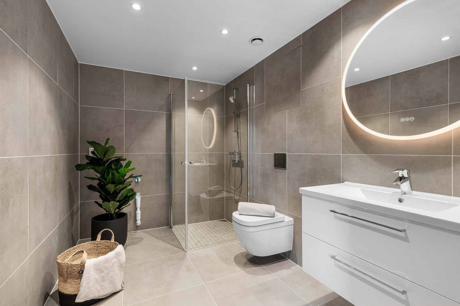 Badet fremstår lyst og moderne med hvit innredning, servant med speil og belysning samt vegghengt toalett og dusjhjørne. Galleribilde