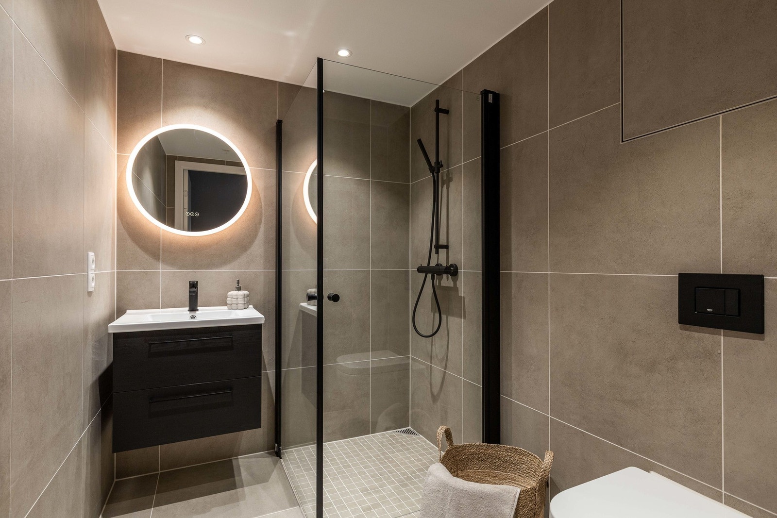 Det andre badet ligger praktisk plassert nær entréen. Her er innredningen mørkere, men uttrykket det samme - helhetlig, moderne og med dusjhjørne, servant med speil og vegghengt toalett. Galleribilde