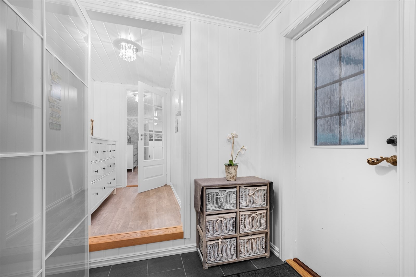 Inngangspartiet er delt i et vindfang med flislagt gulv, gulvvarme og skyvedørsgarderobe, og videre en gang med plass til møblement. Galleribilde