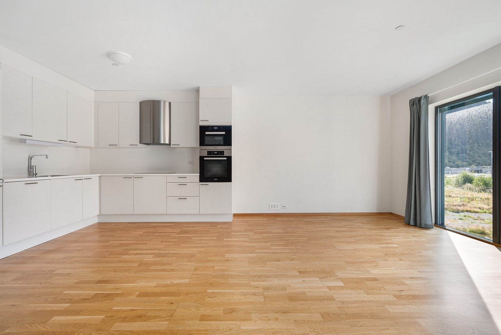 Åpen kjøkkenløsning med innebygde moderne hvitevarer og elegant viftetopp over koketopp. Galleribilde