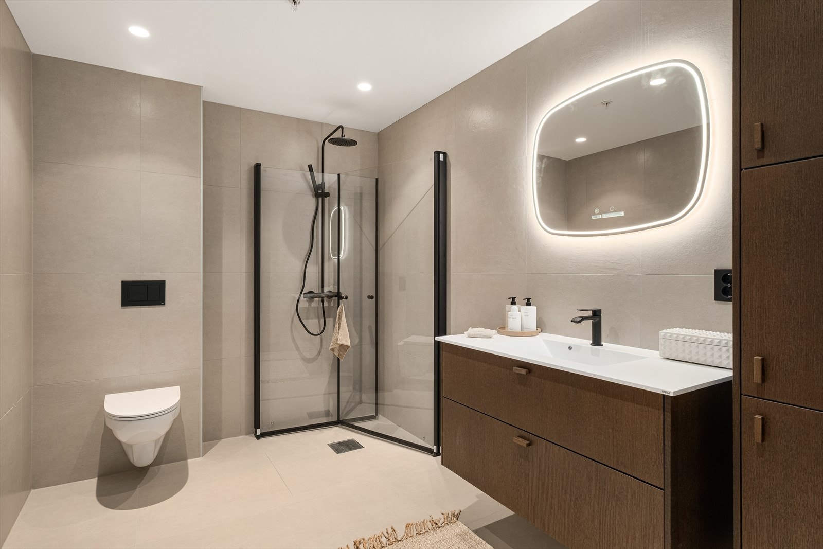 Hovedbadet med med 60x60 Pro Design Ivory på gulv og vegg. Favn Nøtt, Kuma helstøpt benkeplate, lysspeil nature, soft-close toalett og alterna takdusj. Galleribilde