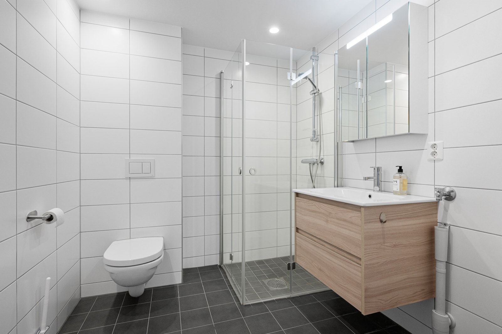 Pent flislagt bad på 4,7 kvm med gulvvarme, downlights og opplegg for vaskemaskin. Videre er badet innredet med servantskap med overskap, dusjhjørne og vegghengt toalett. Galleribilde