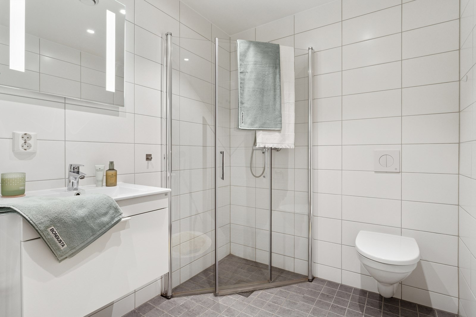 Baderommet har innfellbare dusjvegger av glass, og vegghengt toalett. Pen skuffinnredning med servant og lyssatt speil over. Galleribilde